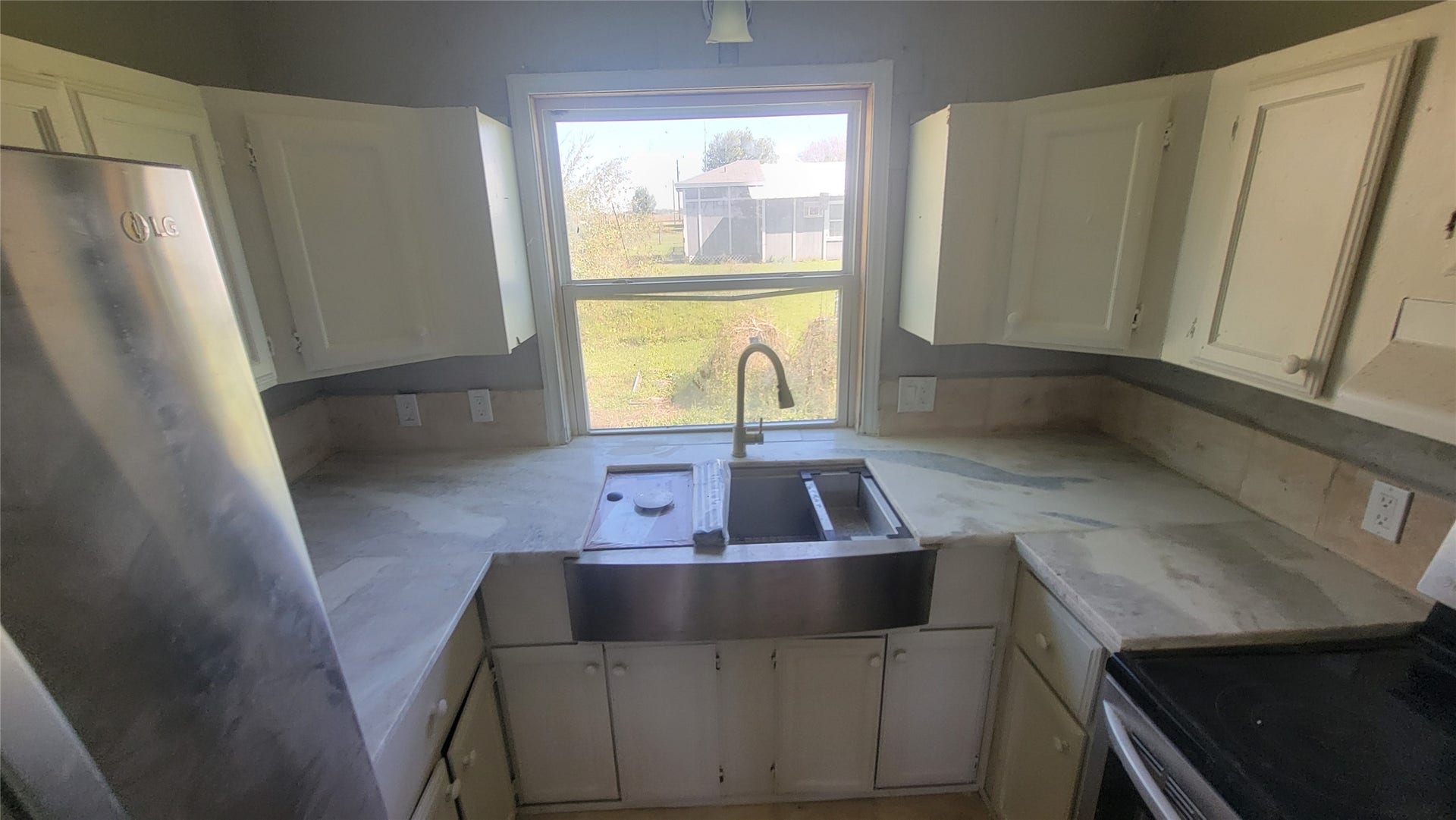 12018 Sandpiper Road, Angleton, TX 77515 This kitchen features a large window overlooking the backyard, white cabinetry, stainless steel appliances, and a farmhouse sink. It offers ample counter space and natural light for a bright, inviting atmosphere.