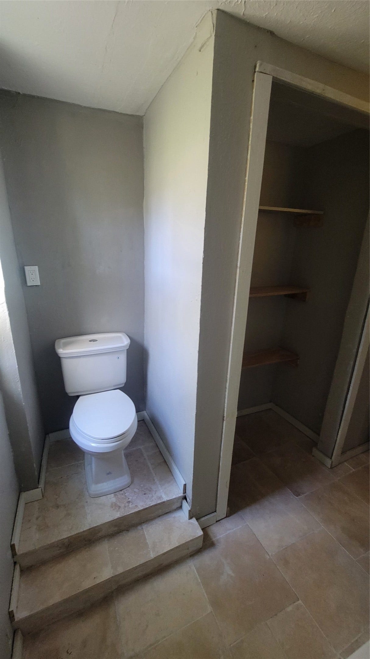 12018 Sandpiper Road, Angleton, TX 77515 This photo shows a compact bathroom area with a raised toilet platform and adjacent shelving space, featuring neutral-colored tiled flooring and walls.
