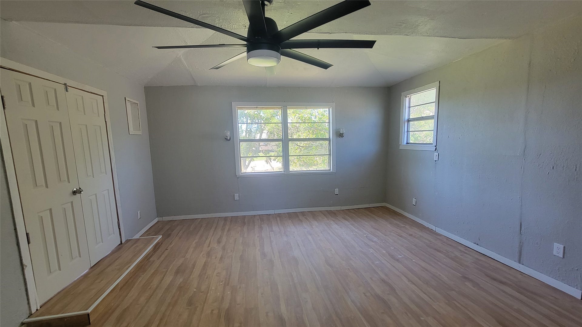 12018 Sandpiper Road, Angleton, TX 77515 Bright room with light wood flooring and neutral gray walls. A large window offers natural light, complemented by a ceiling fan for airflow. There are two additional smaller windows and a double-door closet.