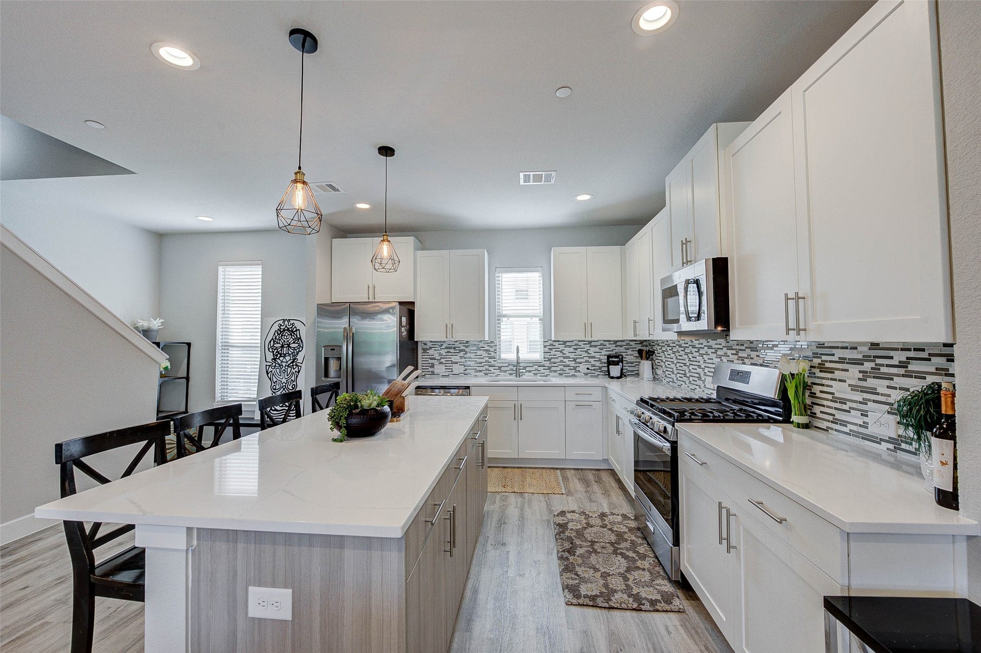 18732 Centro Main Street, Shenandoah, TX 77385 This modern kitchen features sleek white cabinetry, stainless steel appliances, and a stylish tile backsplash. The spacious island offers additional seating and workspace, while pendant lighting adds a warm touch. Natural light fills the room, highlighting the open layout and contemporary design.