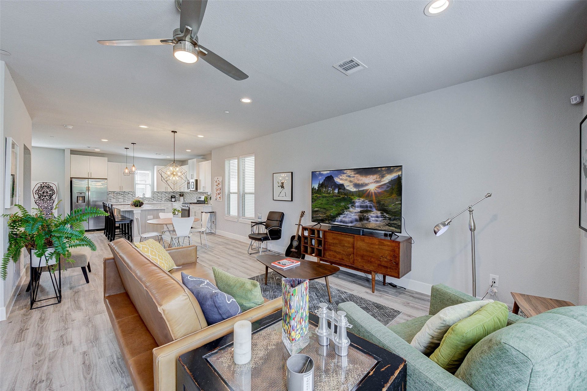 18732 Centro Main Street, Shenandoah, TX 77385 This modern, open-concept living space features a cozy seating area with a stylish sofa, a sleek entertainment setup, and a contemporary kitchen with a breakfast bar. The room is bright and airy, enhanced by recessed lighting and large windows. Perfect for comfortable living and entertaining.