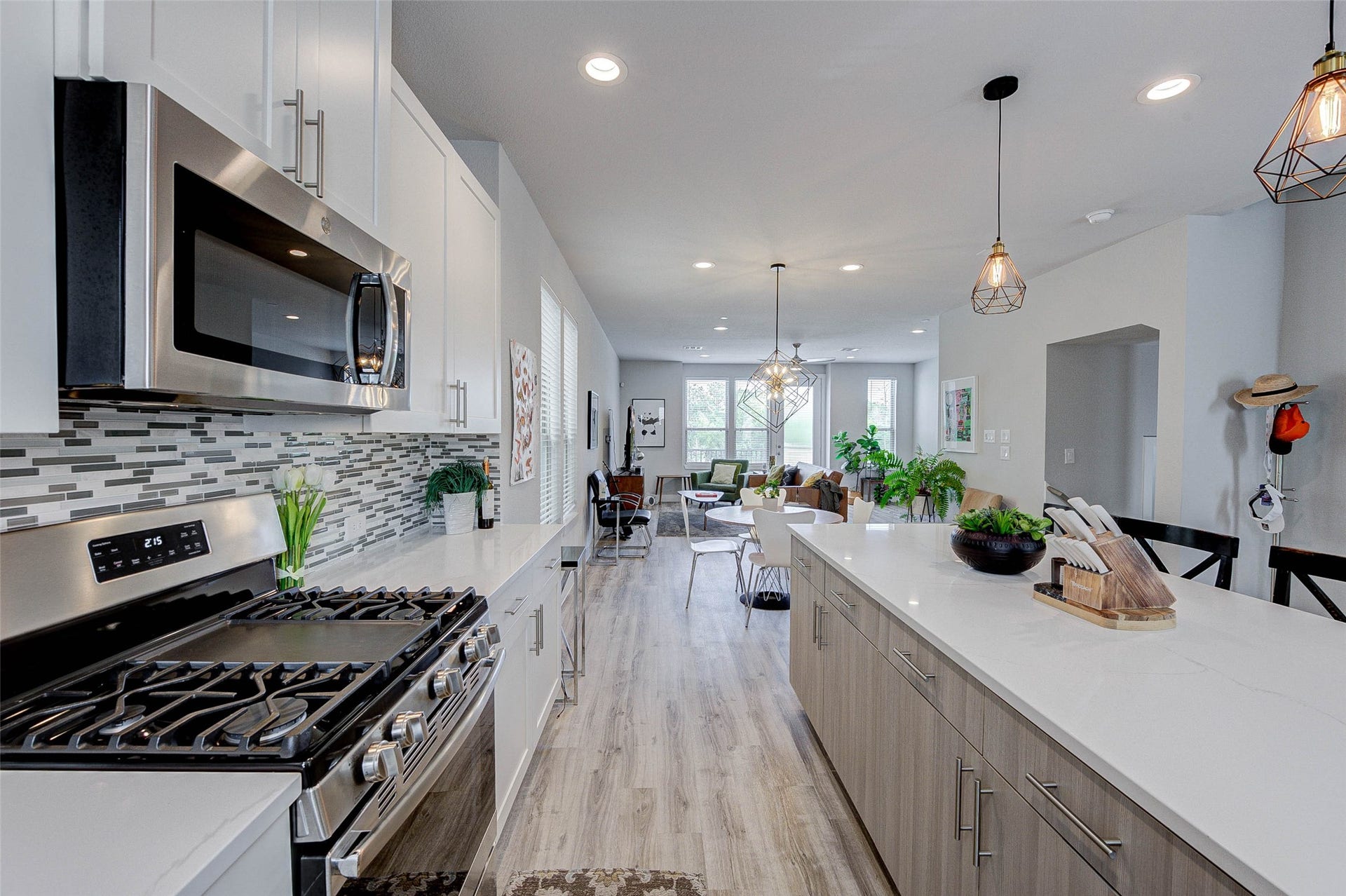 18732 Centro Main Street, Shenandoah, TX 77385 Modern kitchen with sleek stainless steel appliances, a spacious island, and elegant pendant lighting. The open layout extends to a bright living area with large windows, offering a welcoming and airy feel.