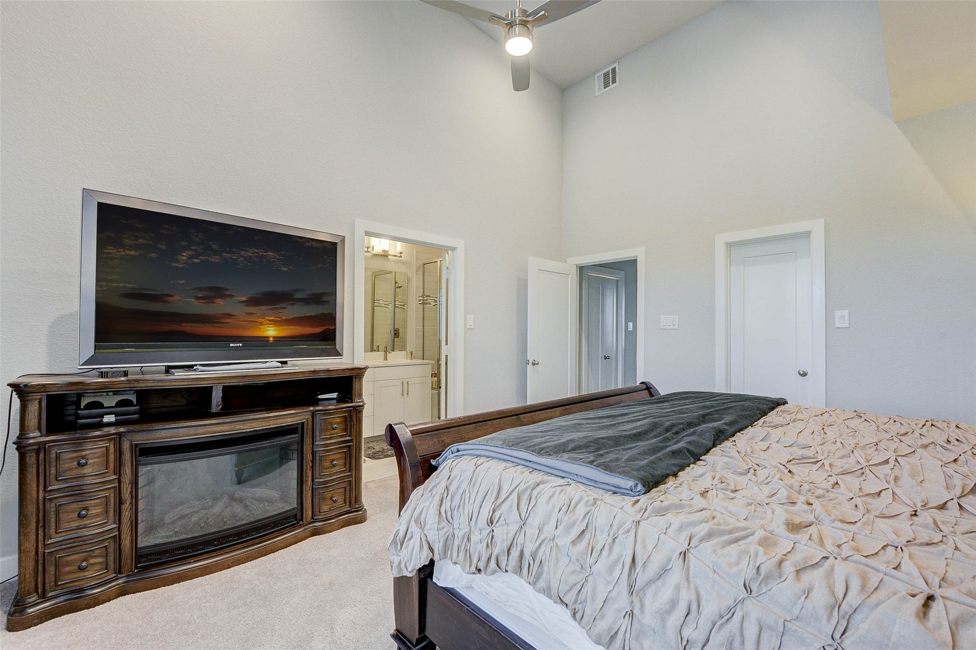 18732 Centro Main Street, Shenandoah, TX 77385 This bedroom features a cozy setup with a stylish wooden TV stand and mounted TV. It has plush carpeting, neutral walls, and a ceiling fan. There's an attached bathroom with modern fixtures, adding convenience and comfort.
