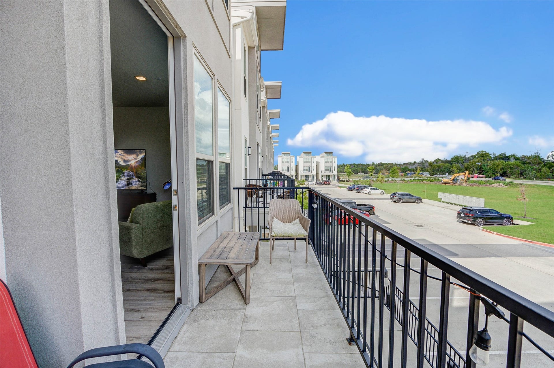 18732 Centro Main Street, Shenandoah, TX 77385 A modern balcony view featuring a spacious area with seating and a scenic outlook over a tidy street and green space. Large windows connect the outdoor and indoor spaces, offering natural light and a contemporary vibe.