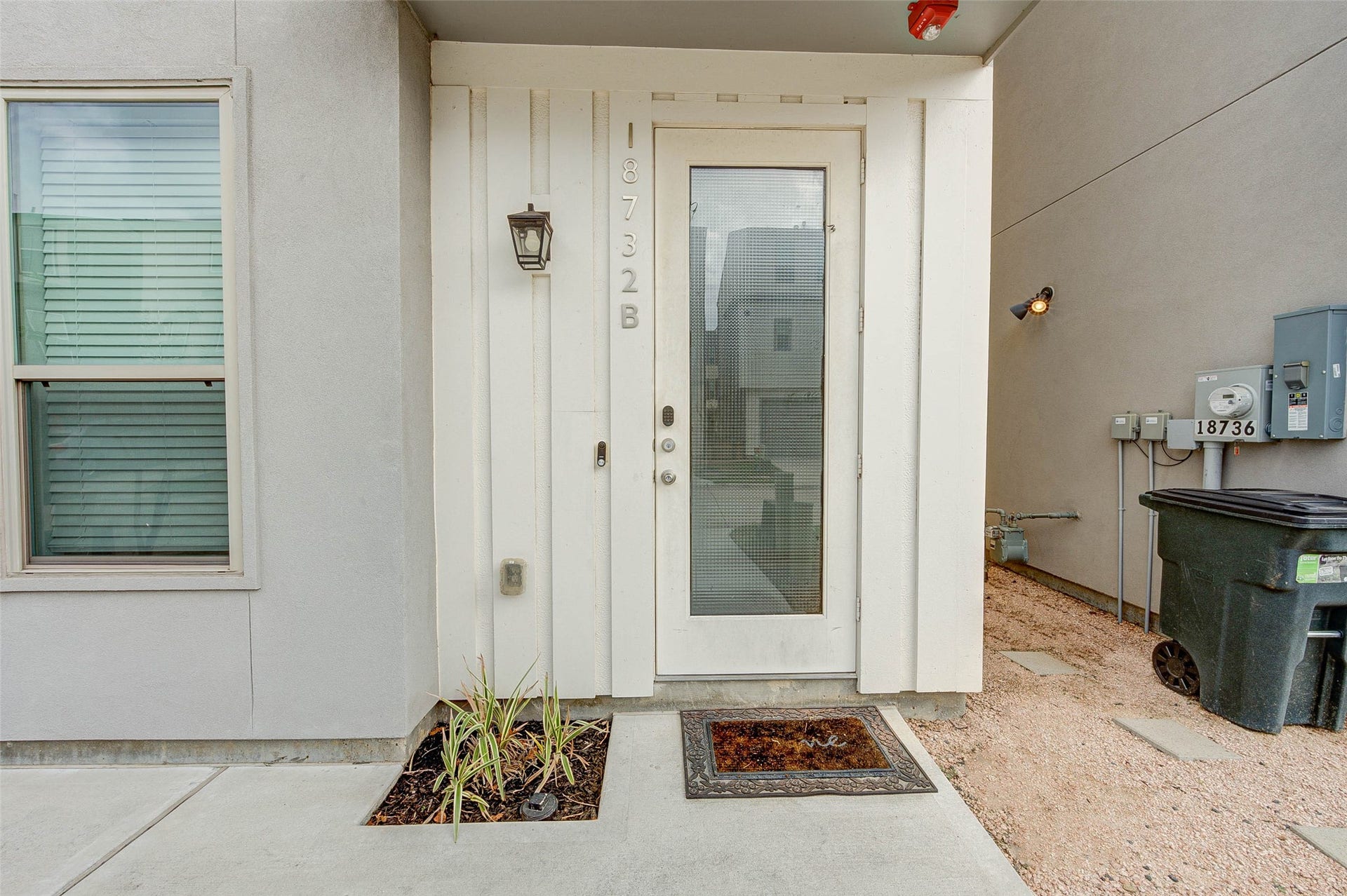 18732 Centro Main Street, Shenandoah, TX 77385 This photo shows a modern entryway with a glass-panel door and a simple exterior light fixture. The area features a small planted bed and a concrete pathway, providing a clean and welcoming entrance.