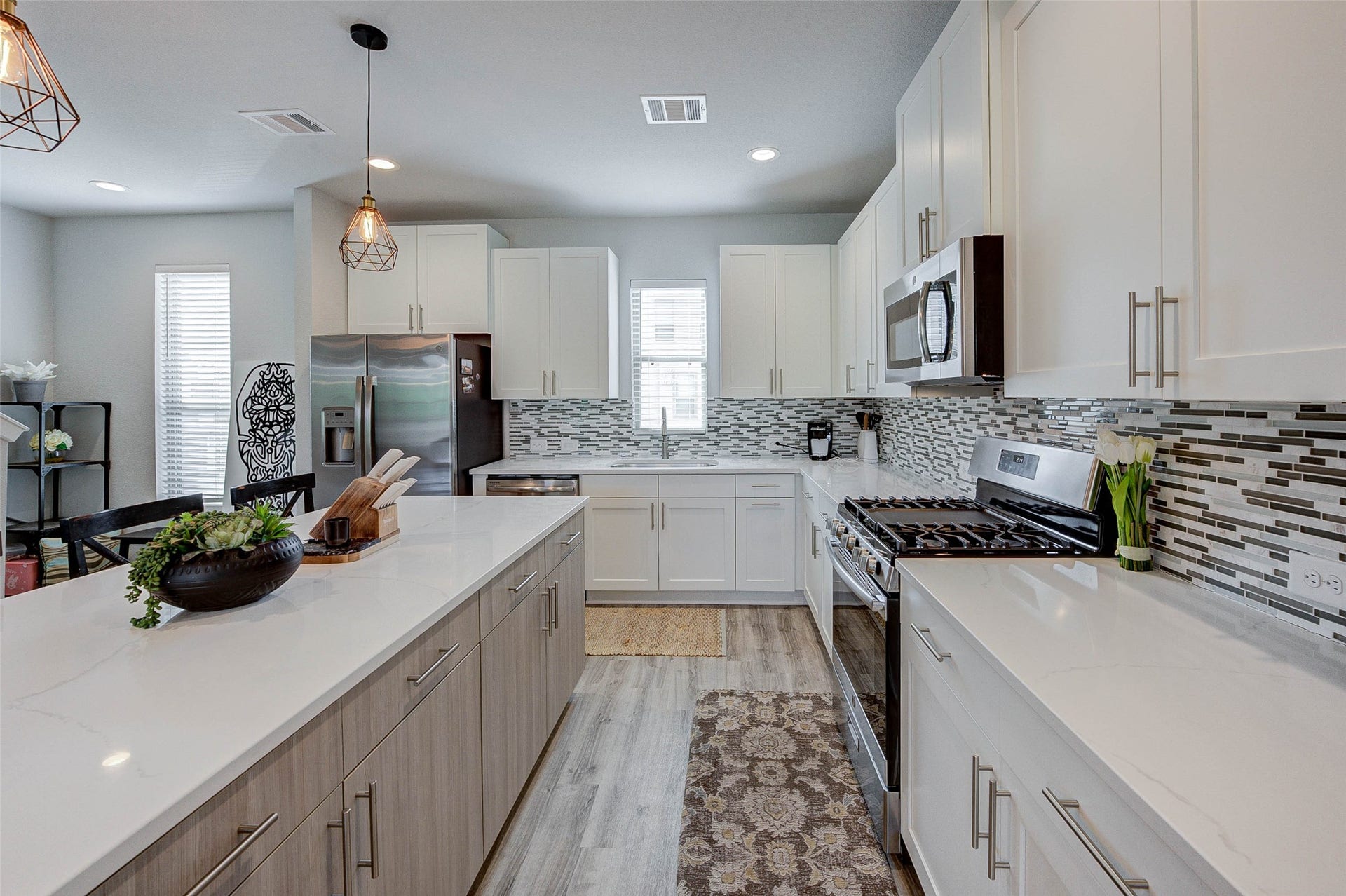18732 Centro Main Street, Shenandoah, TX 77385 This modern kitchen features sleek white cabinetry, a stylish tile backsplash, and stainless steel appliances. It includes a spacious island with ample counter space and elegant pendant lighting, perfect for entertaining.