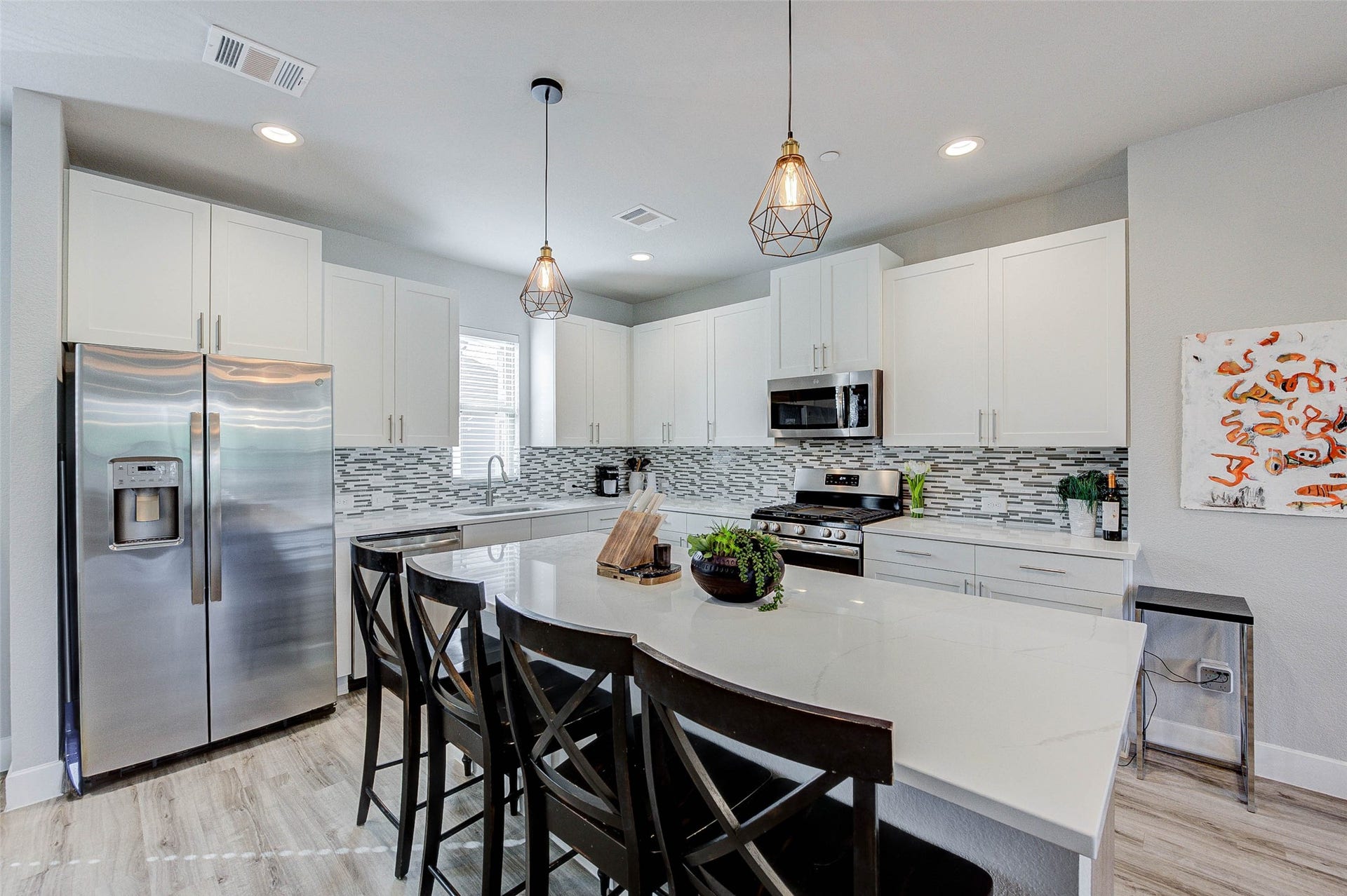 18732 Centro Main Street, Shenandoah, TX 77385 This modern kitchen features sleek white cabinetry, stainless steel appliances, and a stylish tile backsplash. The spacious island with pendant lighting offers additional seating and prep space, perfect for entertaining.