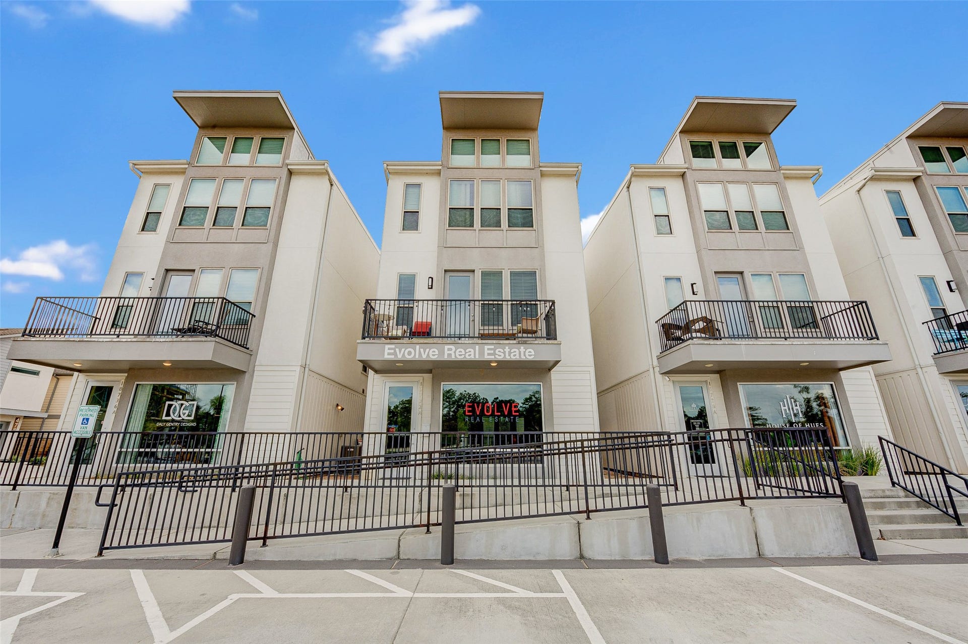 18732 Centro Main Street, Shenandoah, TX 77385 Modern multi-story townhouses with large windows and private balconies, featuring a central real estate office. The building has a clean, contemporary design with a welcoming entrance and ample parking space.