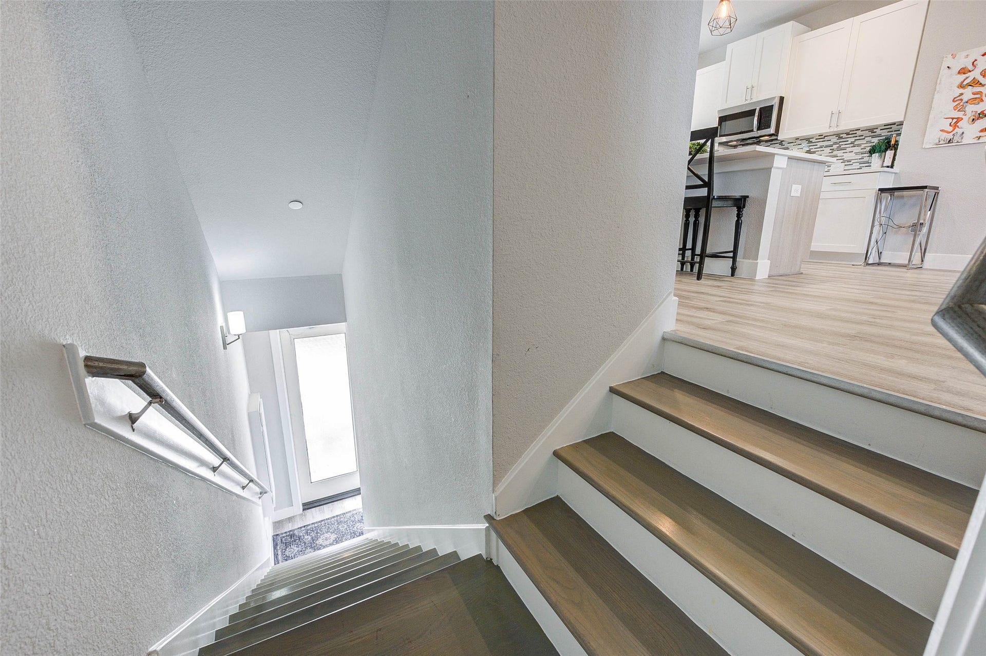 18732 Centro Main Street, Shenandoah, TX 77385 This photo shows a staircase leading to a bright, modern kitchen area with light wood flooring, white cabinetry, and a decorative backsplash. The space is open and inviting, with contemporary design elements.