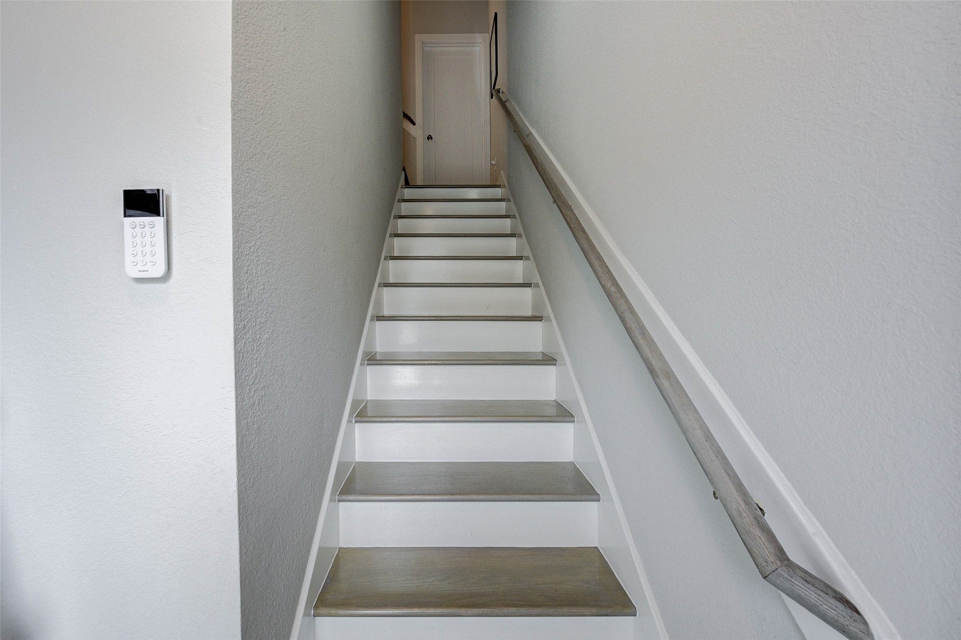 18732 Centro Main Street, Shenandoah, TX 77385 This photo shows a narrow staircase with a wooden handrail leading to a door at the top. The walls are painted white, and a security keypad is mounted on the side wall.