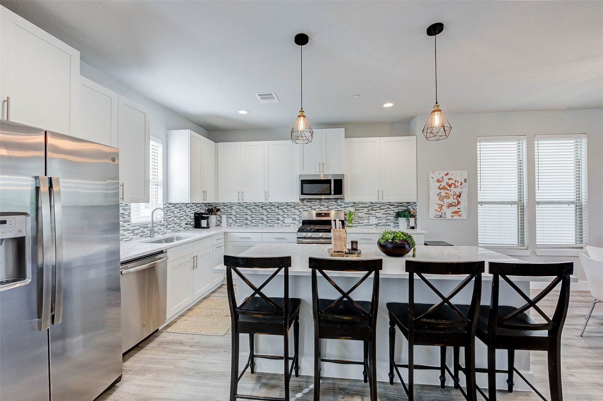 18732 Centro Main Street, Shenandoah, TX 77385 Modern kitchen with sleek white cabinetry, stainless steel appliances, and a stylish backsplash. The island features seating for four and contemporary pendant lighting. Spacious and bright with plenty of windows.