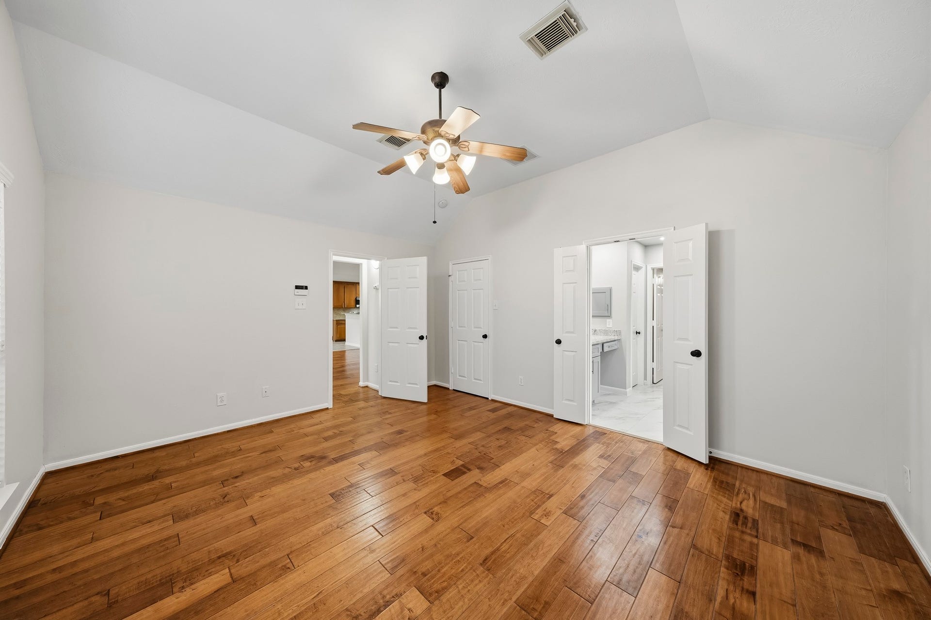 Spacious Spacious primary retreat with wood floors, vaulted ceiling, ceiling fan, and large windows that flood the room with natural light. This serene sanctuary offers ample space for a sitting area, walk-in closets, and an en-suite bathroom.