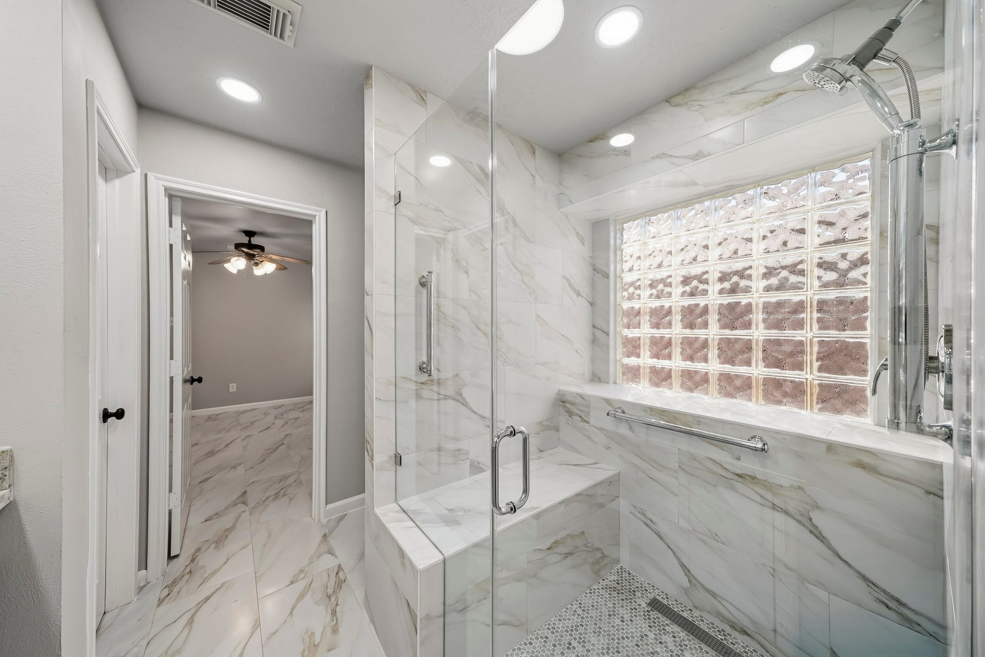 Spacious walk-in shower featuring custom modern tilework, an integrated bench, and an elegant tile surround accented by a glass block window for natural light.