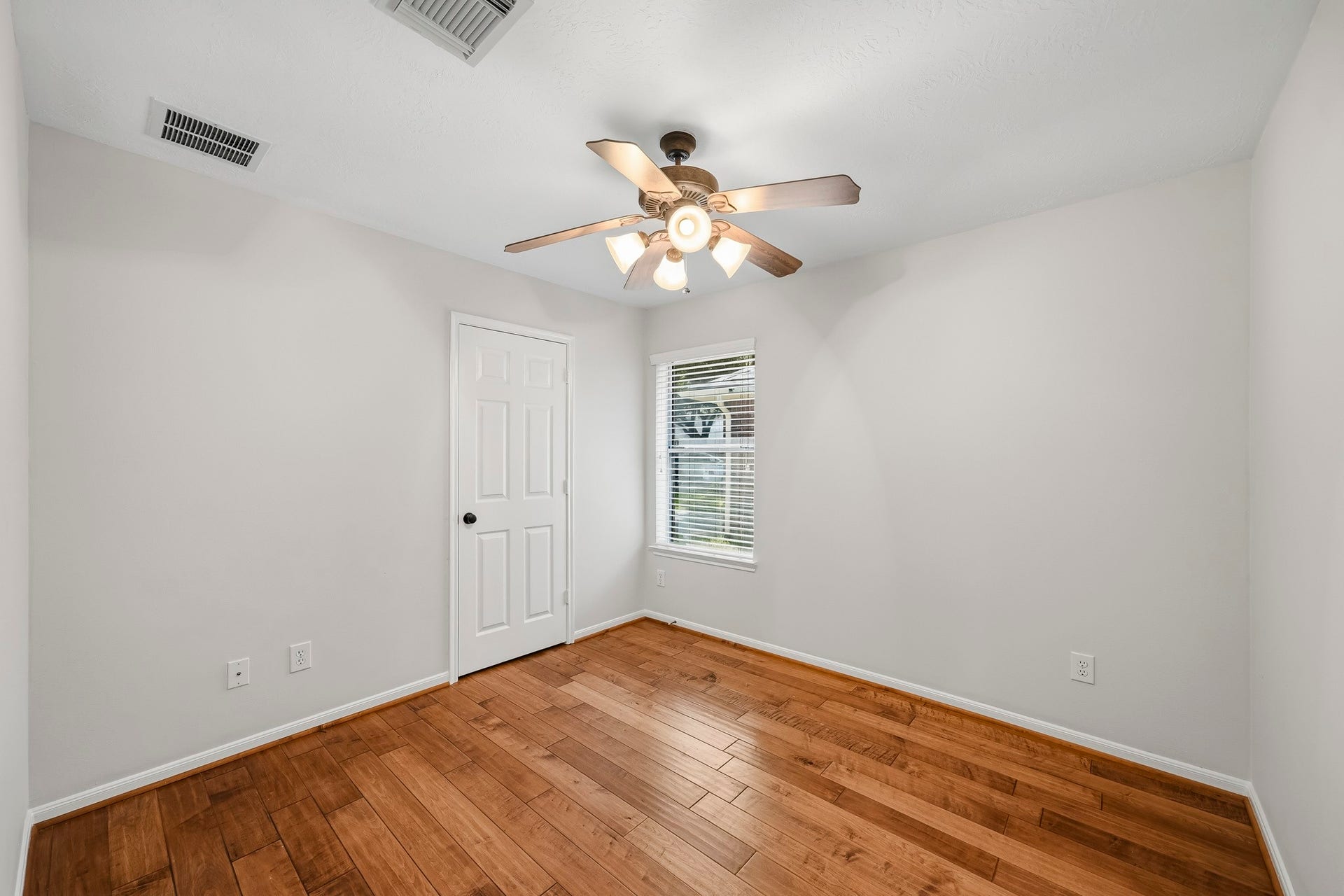 Spacious second bedroom featuring gleaming hardwood floors, an updated ceiling fan, and fresh neutral paint throughout.