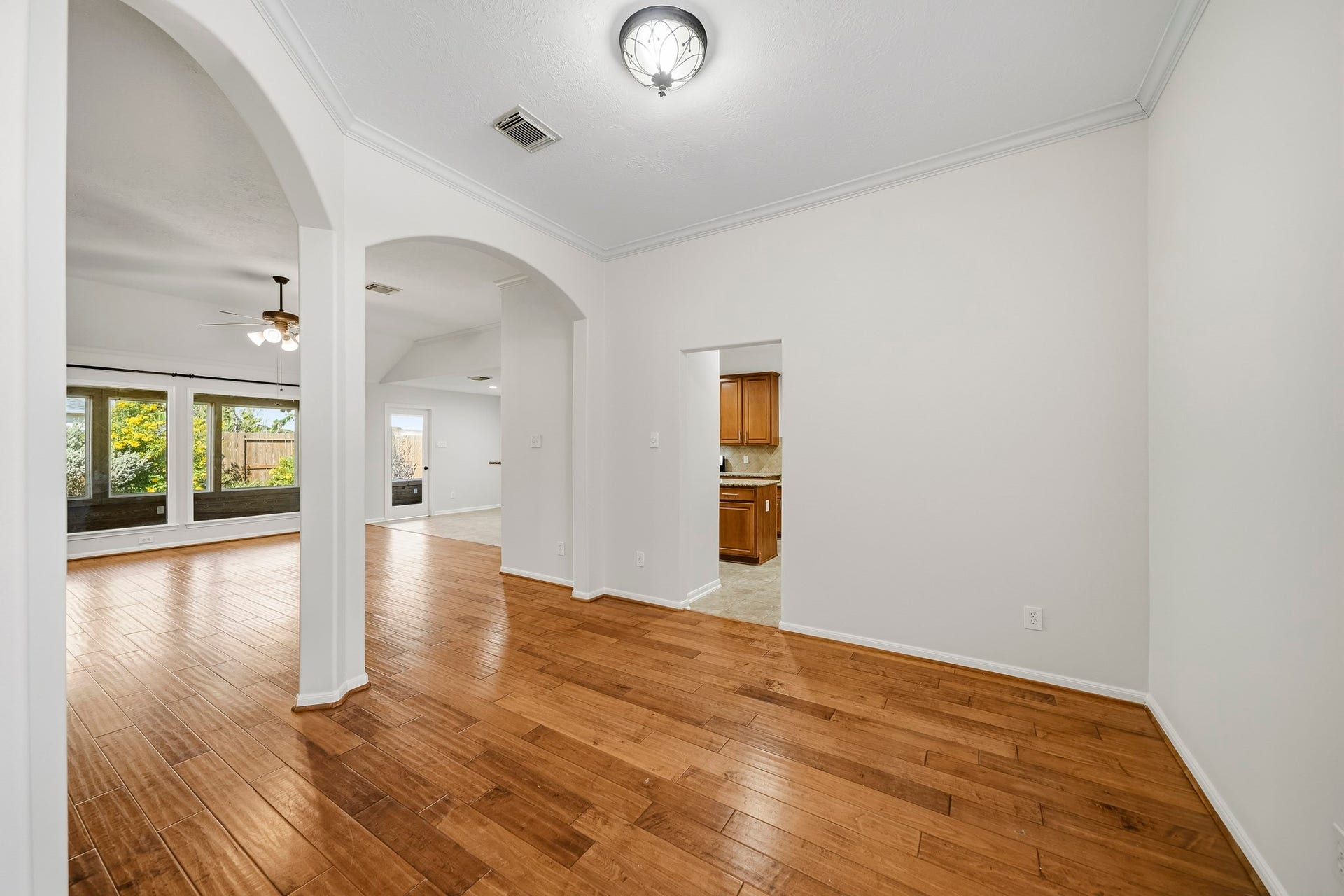 Formal dining room featuring an open-concept flow into the main living area, accented by elegant arches, architectural columns, crown molding, and beautiful hardwood flooring.