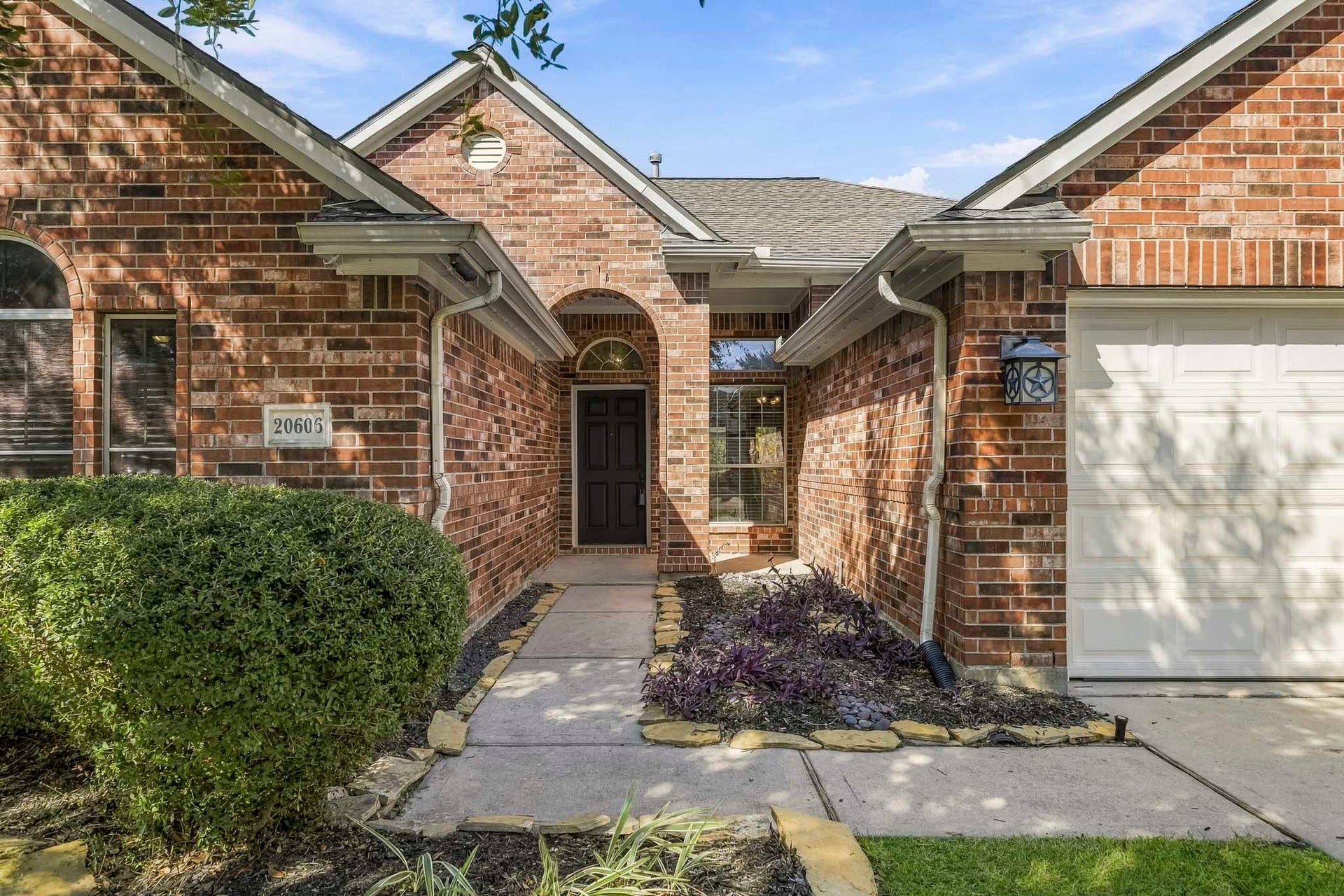 Lovely one-story brick home featuring a welcoming entry framed by established, lush landscaping.