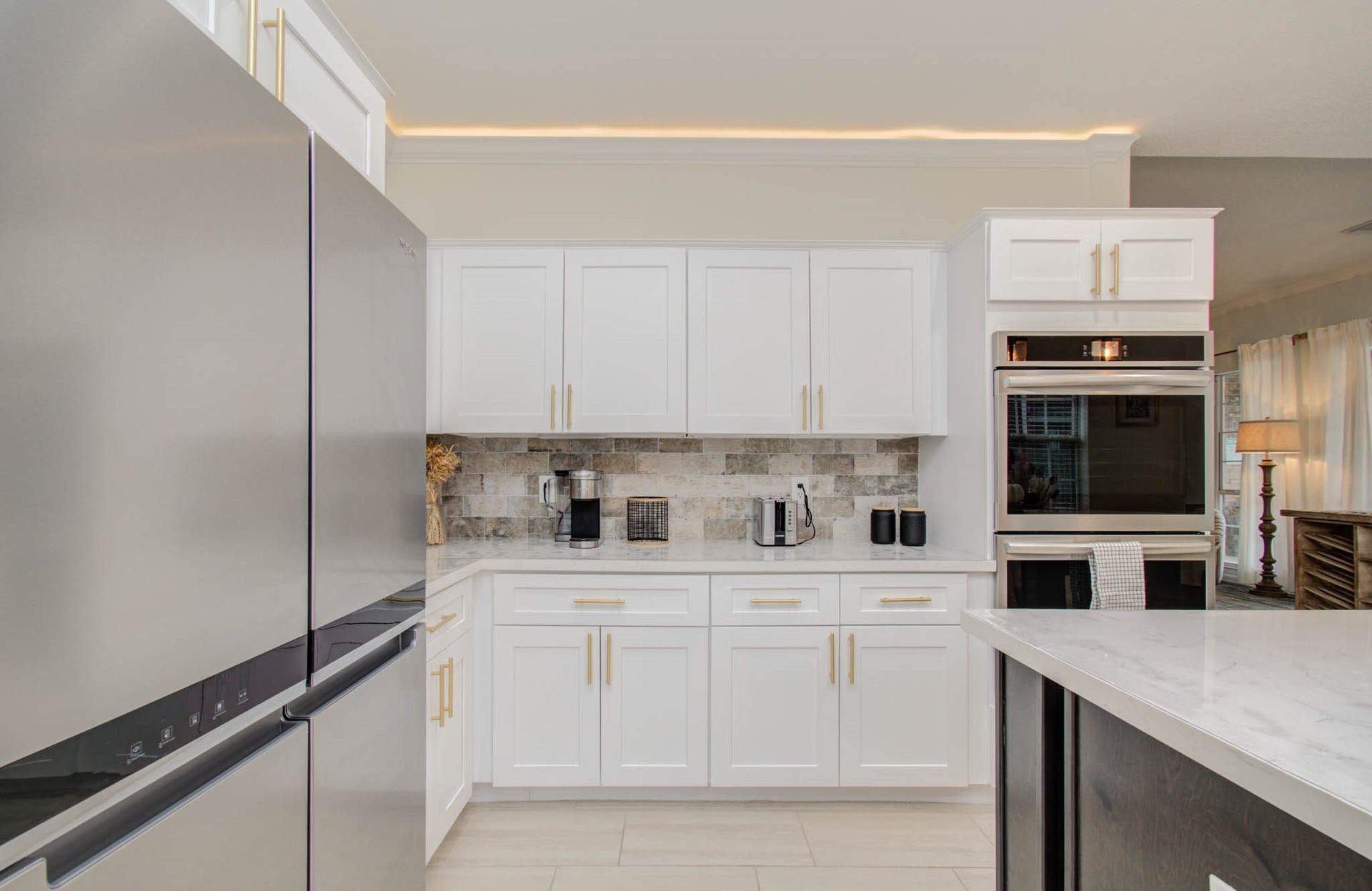 15627 Twisting Springs Drive, Cypress, TX 77433 Modern kitchen featuring sleek stainless steel appliances, elegant white cabinetry with gold hardware, and a stylish stone backsplash, offering a bright and contemporary cooking space.