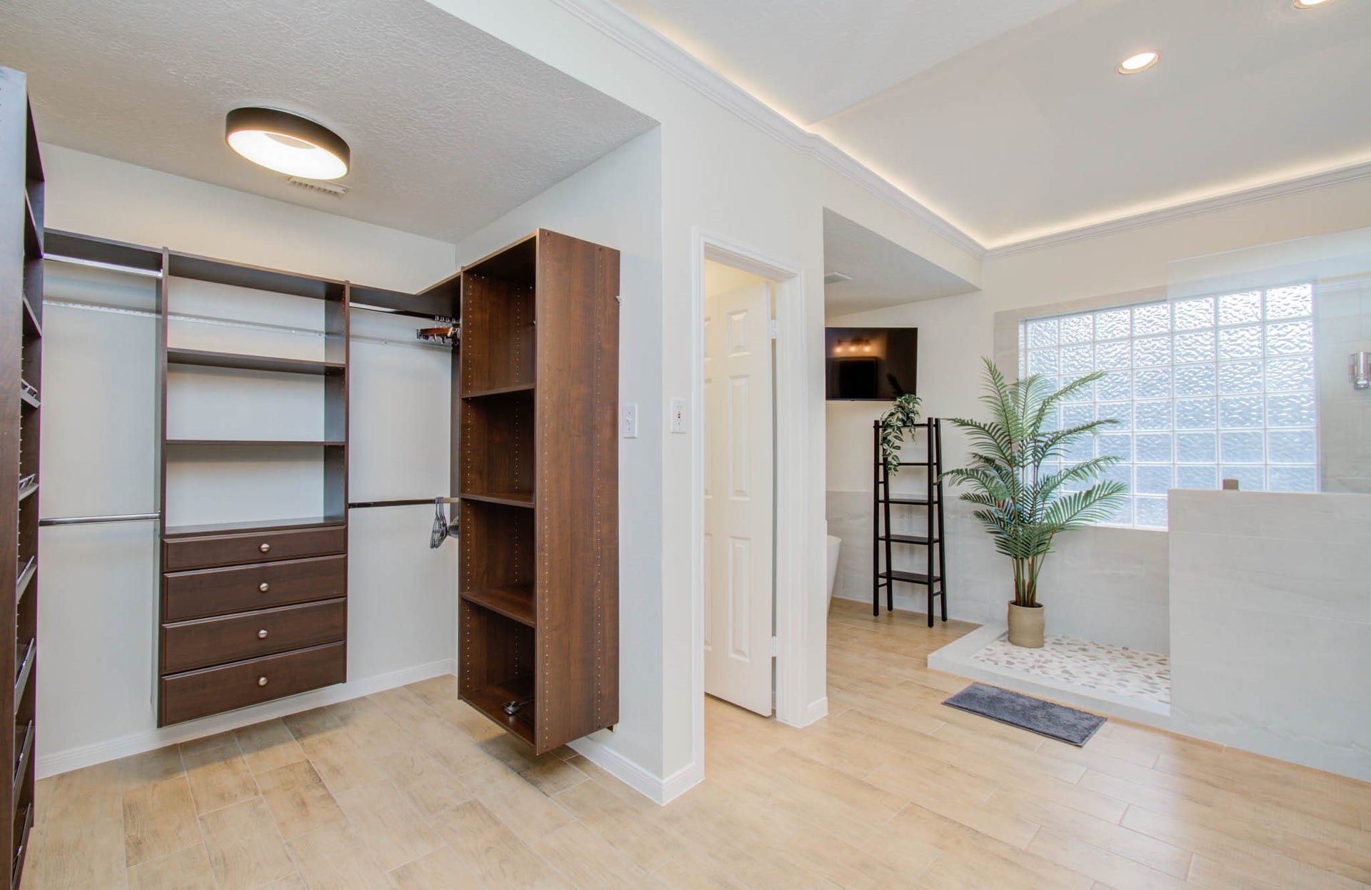15627 Twisting Springs Drive, Cypress, TX 77433 Spacious walk-in closet with custom shelving and drawers, adjacent to a modern bathroom featuring a glass block window and stylish tile flooring.