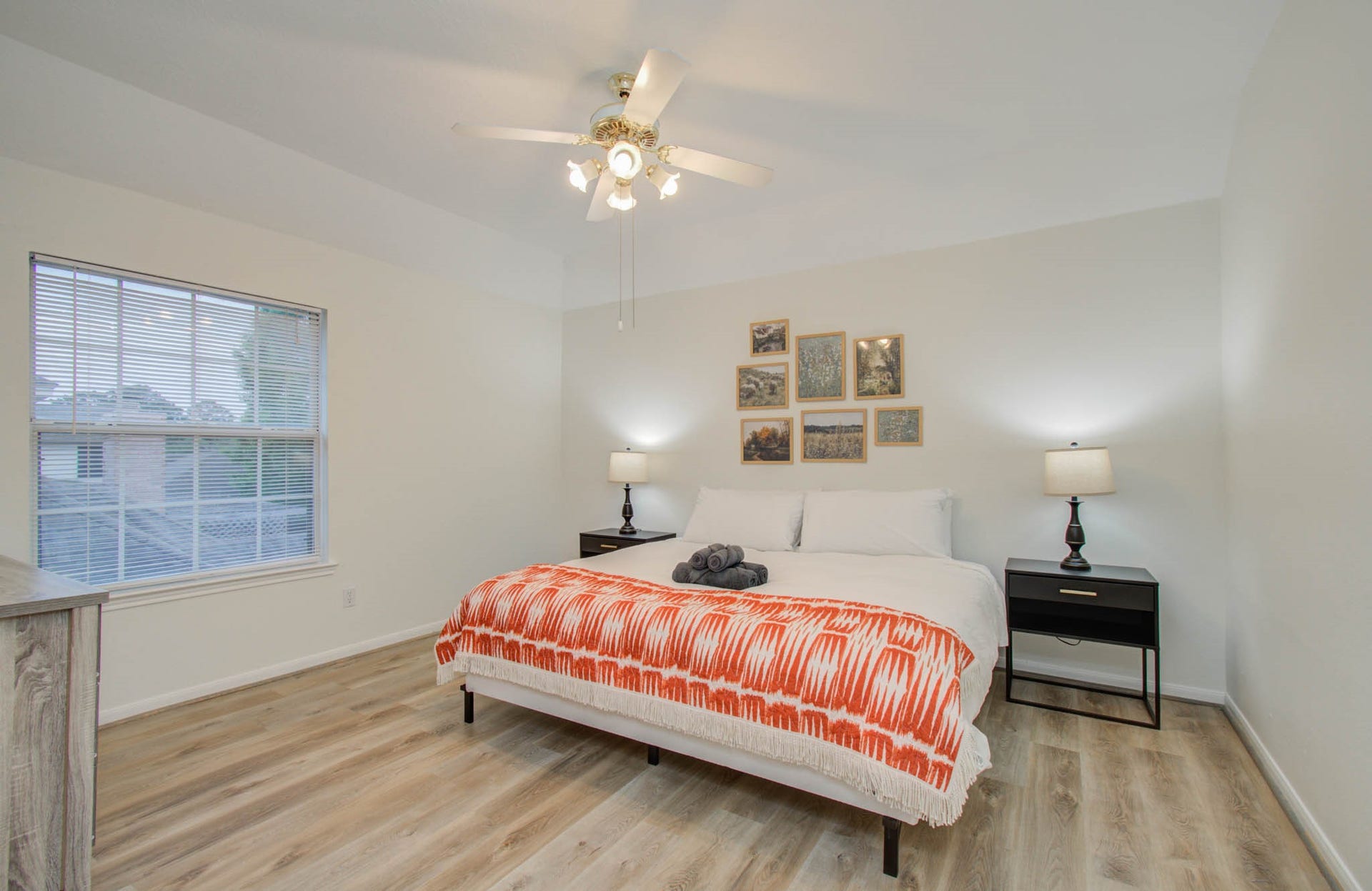 15627 Twisting Springs Drive, Cypress, TX 77433 Spacious bedroom with elegant hardwood floors, a cozy bed adorned with a vibrant orange throw, and abundant natural light from a large window.