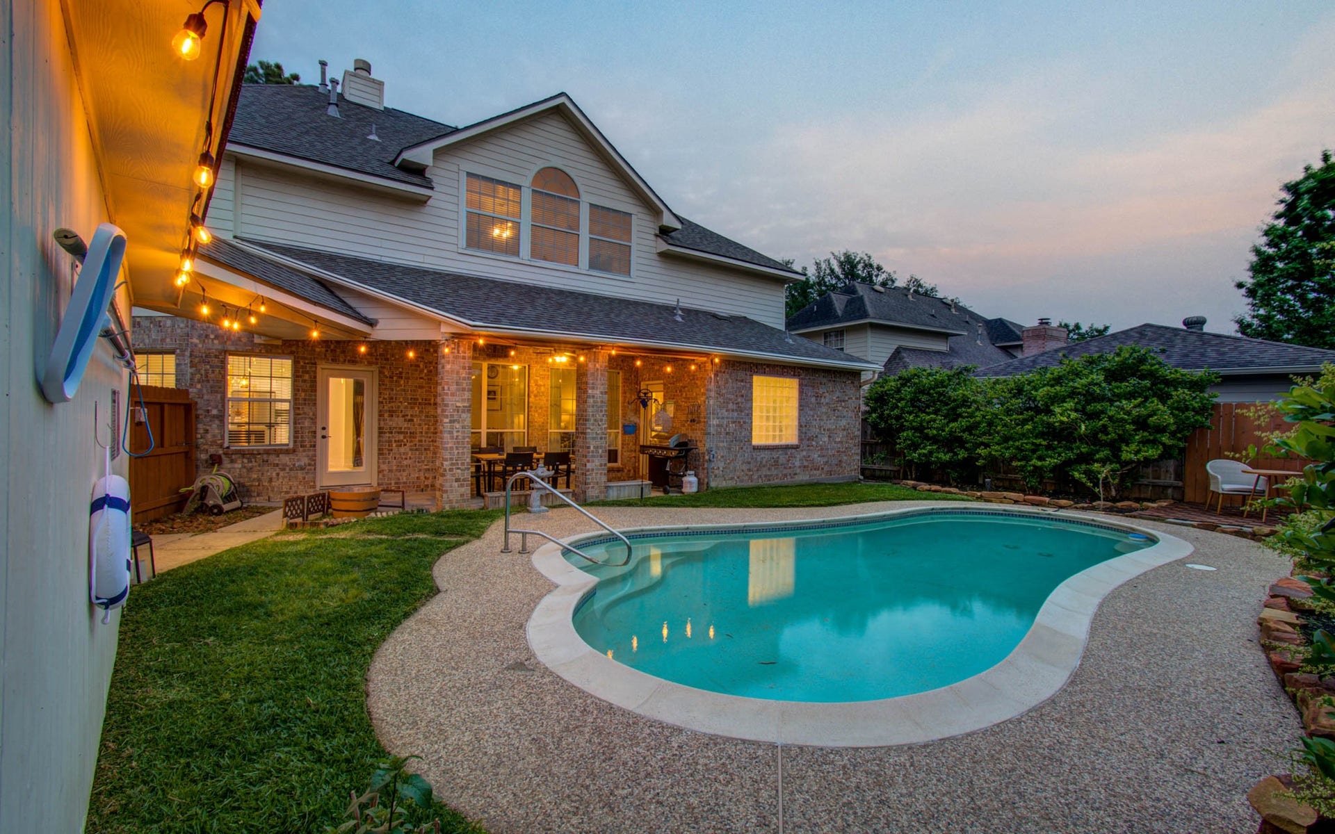 15627 Twisting Springs Drive, Cypress, TX 77433 Charming backyard oasis featuring a sparkling pool surrounded by lush greenery and cozy patio lighting, perfect for evening relaxation and entertaining.
