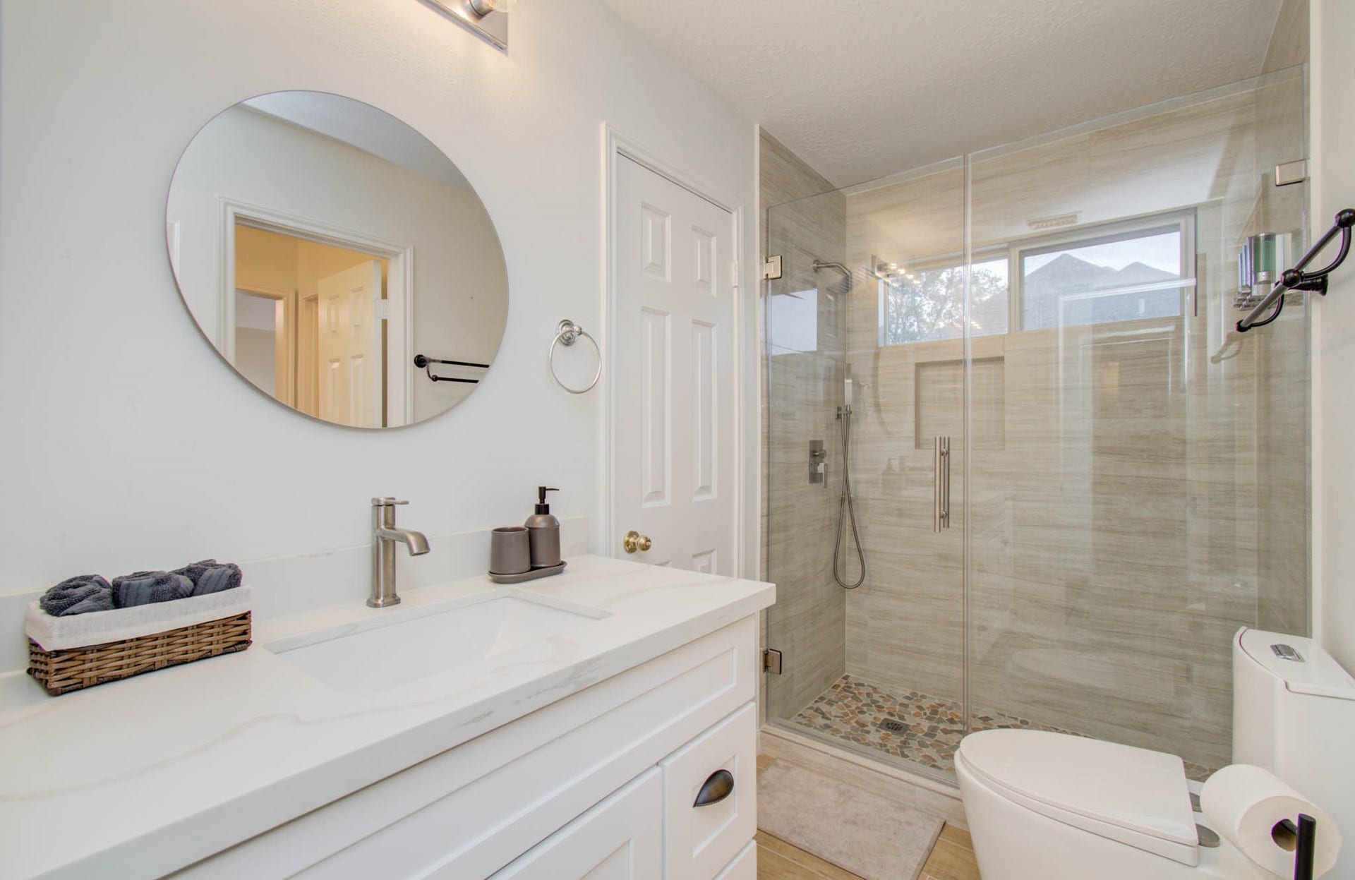 15627 Twisting Springs Drive, Cypress, TX 77433 Modern bathroom featuring a sleek glass-enclosed shower with pebble floor, elegant vanity with a round mirror, and contemporary fixtures for a luxurious feel.