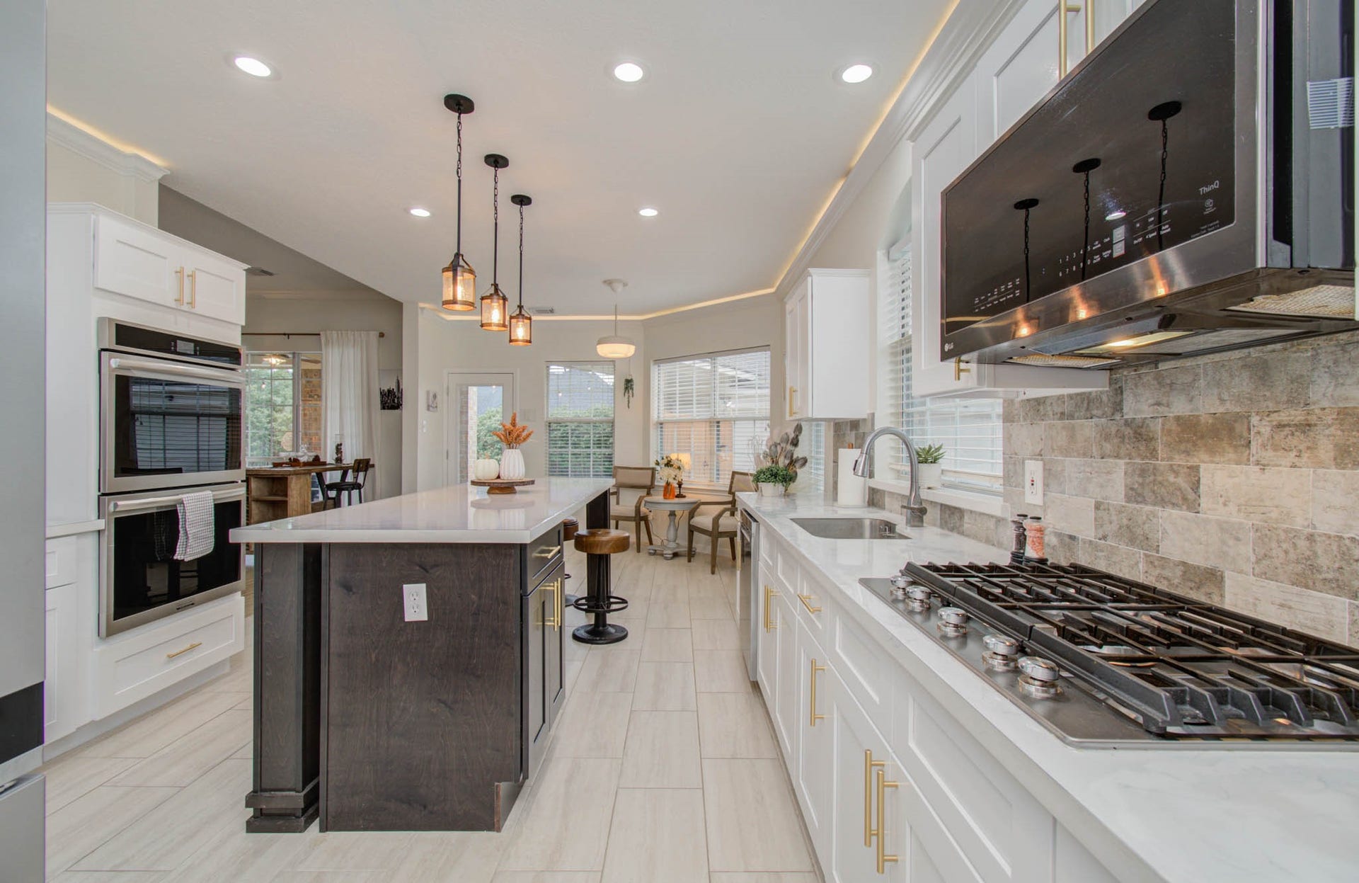 15627 Twisting Springs Drive, Cypress, TX 77433 Modern kitchen with sleek white cabinetry, a spacious island with pendant lighting, and high-end stainless steel appliances, including a gas cooktop and double ovens.