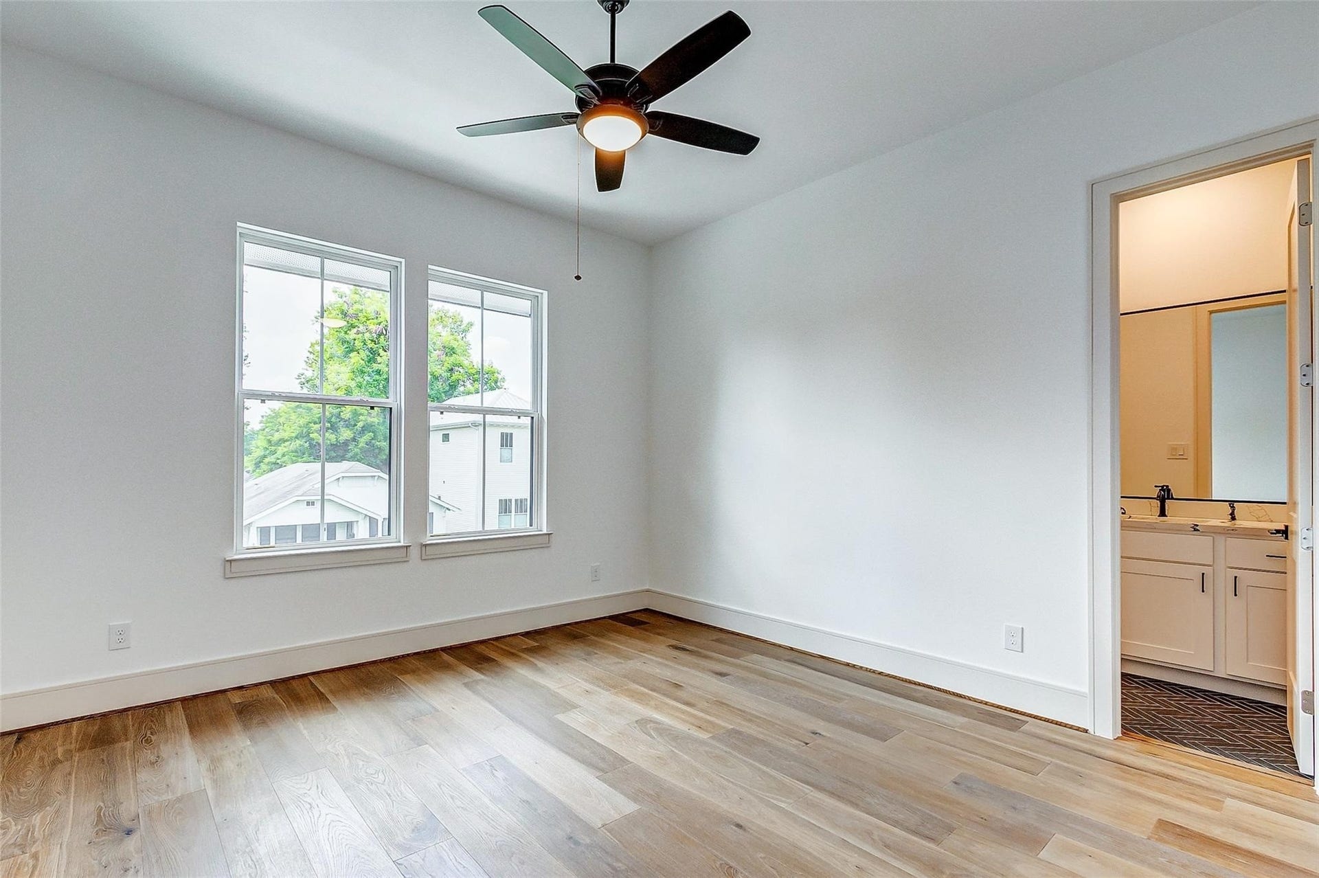 605 E 26th A Street, Houston, TX 77008 Bright bedroom with hardwood floors, large windows, and a ceiling fan, leading to an en-suite bathroom.
