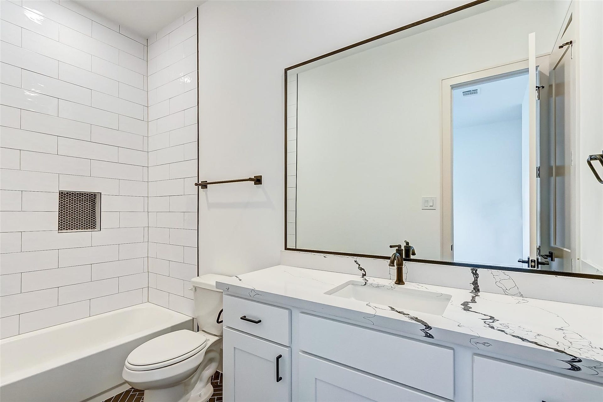 605 E 26th A Street, Houston, TX 77008 Modern bathroom featuring quartz countertop, large mirror, elegant fixtures, and a stylish subway-tiled shower.