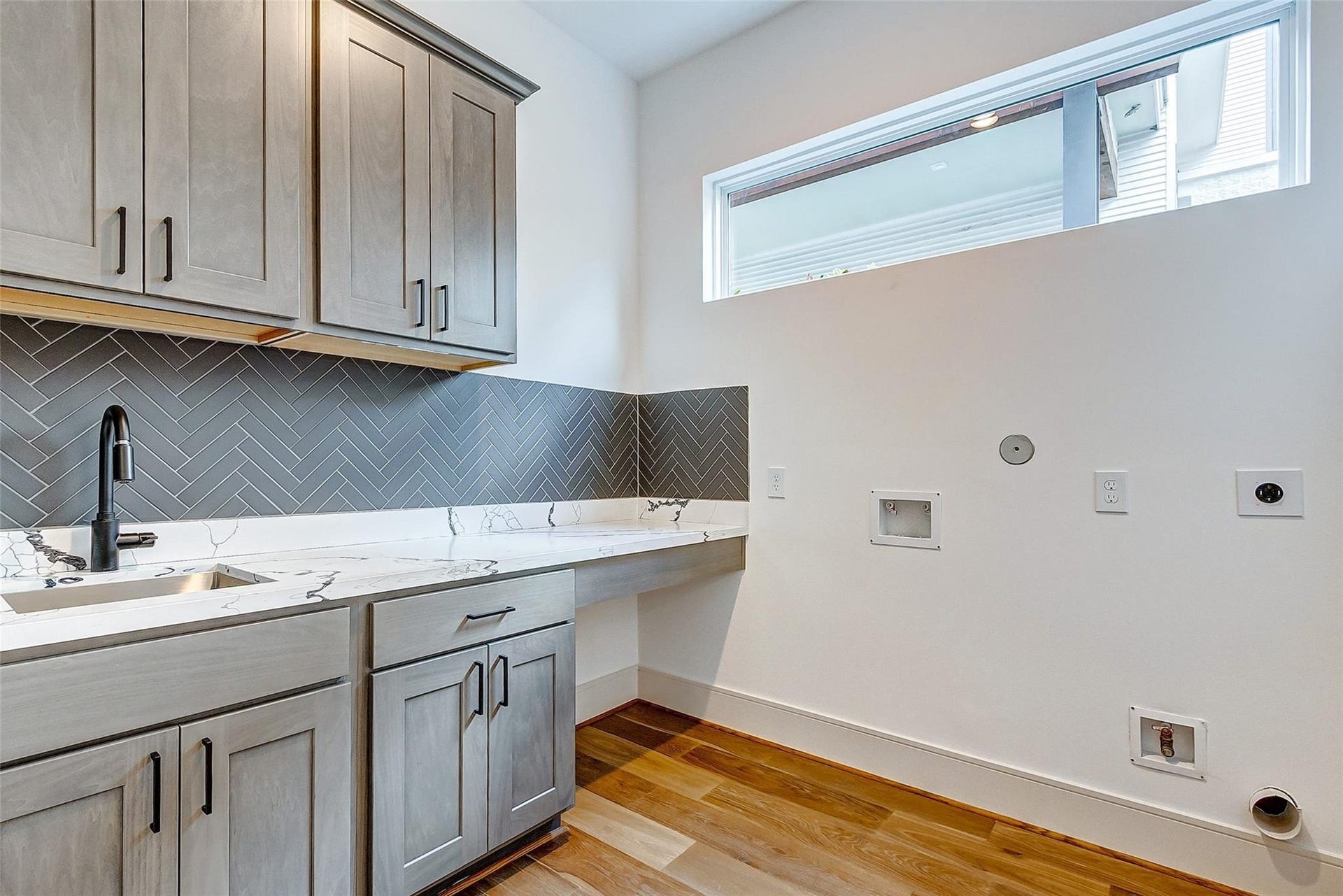 605 E 26th A Street, Houston, TX 77008 Chic laundry room featuring sleek cabinetry, a sink, modern herringbone backsplash, and a spacious countertop, complemented by ample natural light.