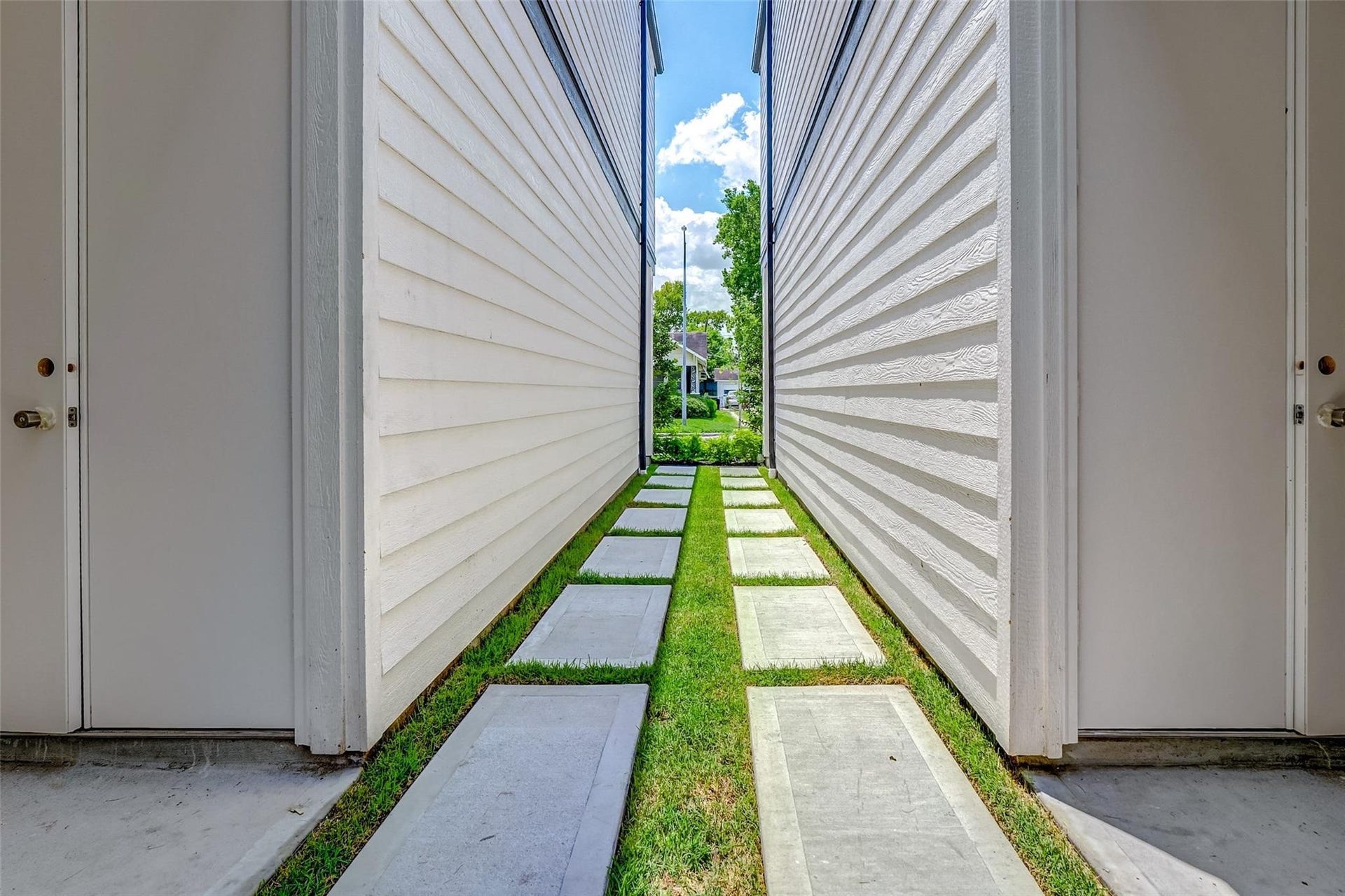 605 E 26th A Street, Houston, TX 77008 Charming walkway nestled between two buildings, featuring sleek horizontal siding and a modern path of concrete slabs set in lush green grass.