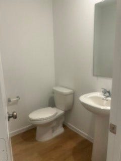 Charming half-bath featuring a modern pedestal sink, sleek mirror, and elegant wood flooring, perfect for guests.