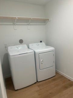 Bright laundry room featuring modern washer and dryer set, with convenient overhead shelving and sleek wood flooring.