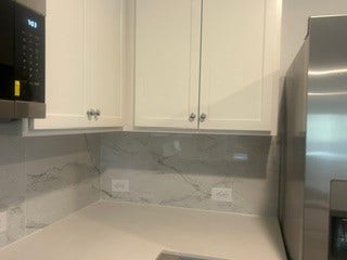 Sleek kitchen corner featuring modern white .tall cabinetry, elegant marble-style backsplash, and a stainless steel refrigerator.