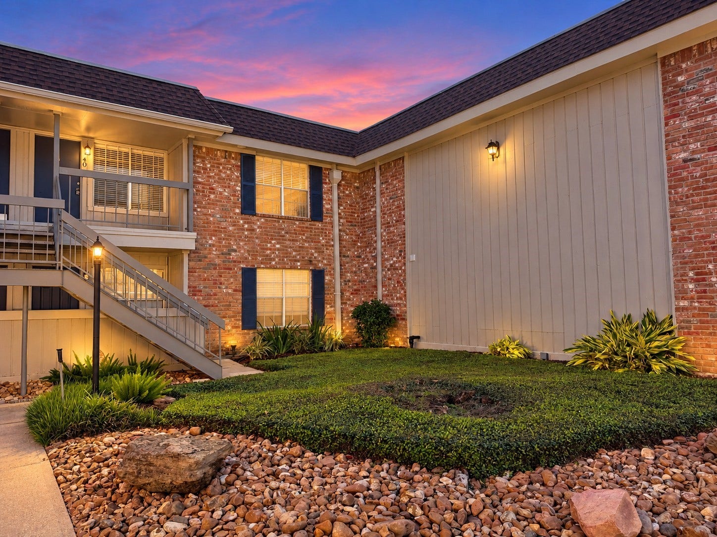 2250 Bering Drive, #40, Houston, TX 77057 Twilight Enhanced: Charming brick exterior overlooking a landscaped courtyard with mature greenery and decorative stone accents. Twilight-enhanced photography highlights the welcoming exterior and second-floor access.