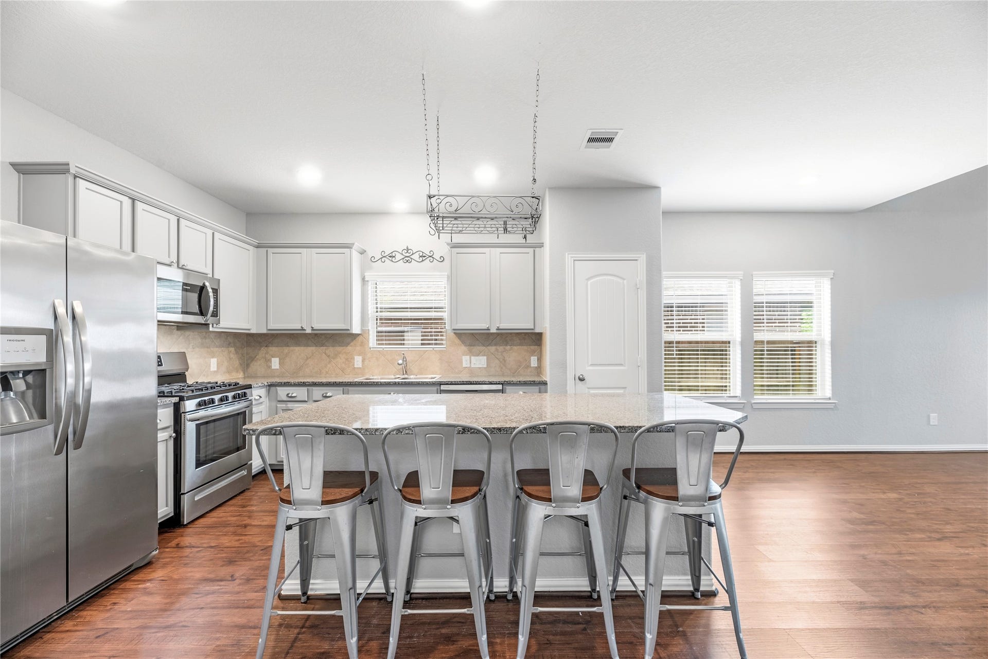 6418 Shadowbrook Hollow Trail, Katy, TX 77493 The kitchen features granite countertops, a massive central island with breakfast bar seating, light gray cabinetry with modern hardware, and high-end stainless steel appliances, including a gas cooktop and oven.