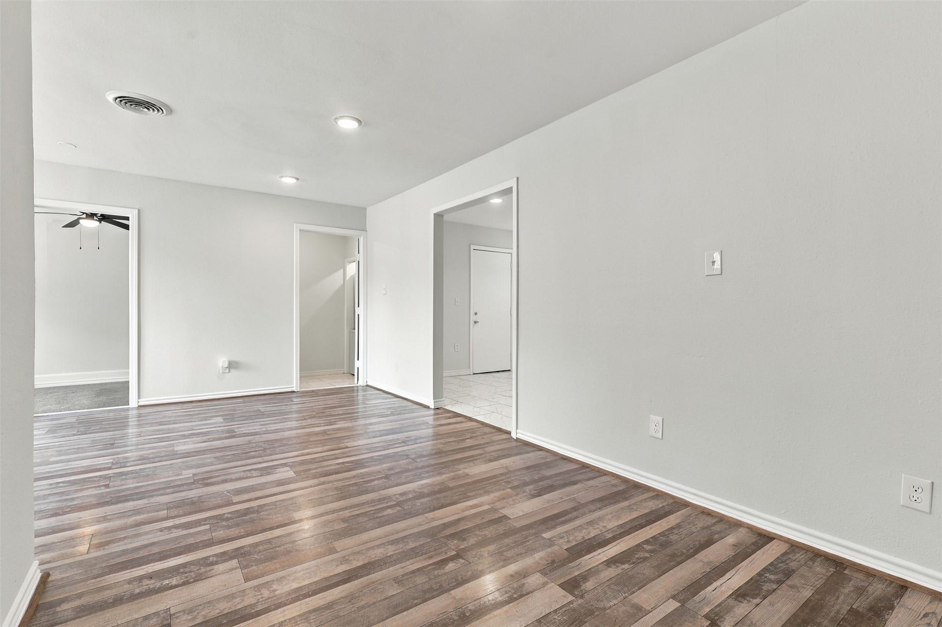 Take a look at this spacious living area! Beautiful wood-look laminate flooring, high ceilings, and recessed lighting create a bright and welcoming atmosphere. The thoughtfully arranged layout provides convenient access to the bedrooms, while the doorway on the right leads to the dining area, making everyday living and entertaining a breeze!