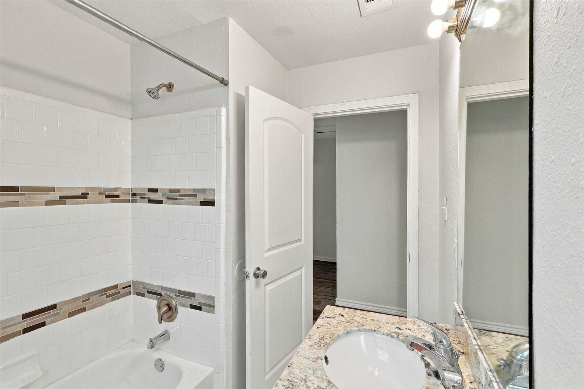 Another lovely view of the secondary bathroom! Featuring a tub-and-shower combination with attractive tiled walls, decorative accent details, and a granite vanity countertop, this bright and practical space offers comfort and convenience for the whole family.