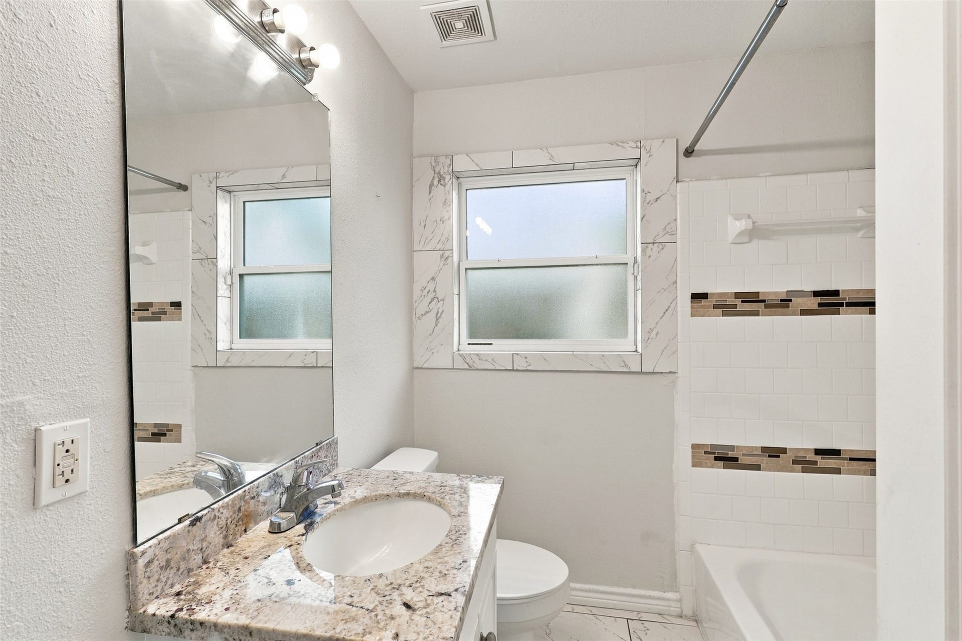 Bright, clean, and ready for everyday living! The secondary bathroom features a granite vanity countertop, generous mirror, natural light, and a tub-and-shower combination with attractive tile surround. A practical and refreshing space designed to make busy mornings and evening routines a little easier.