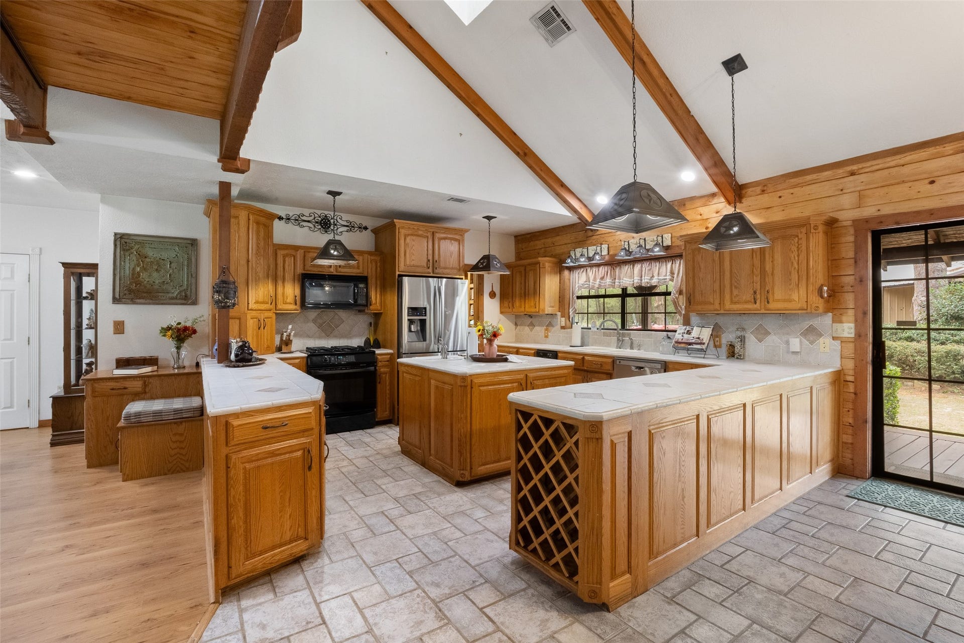 27874 Riley Road, Waller, TX 77484 The spacious kitchen and dining area offers plenty of room to cook, gather and entertain, with beautiful Amish-built cabinetry, soaring ceilings and exposed wood beams. Tile countertops and backsplash, black and stainless-steel appliances and abundant storage make this kitchen as functional as it is inviting.