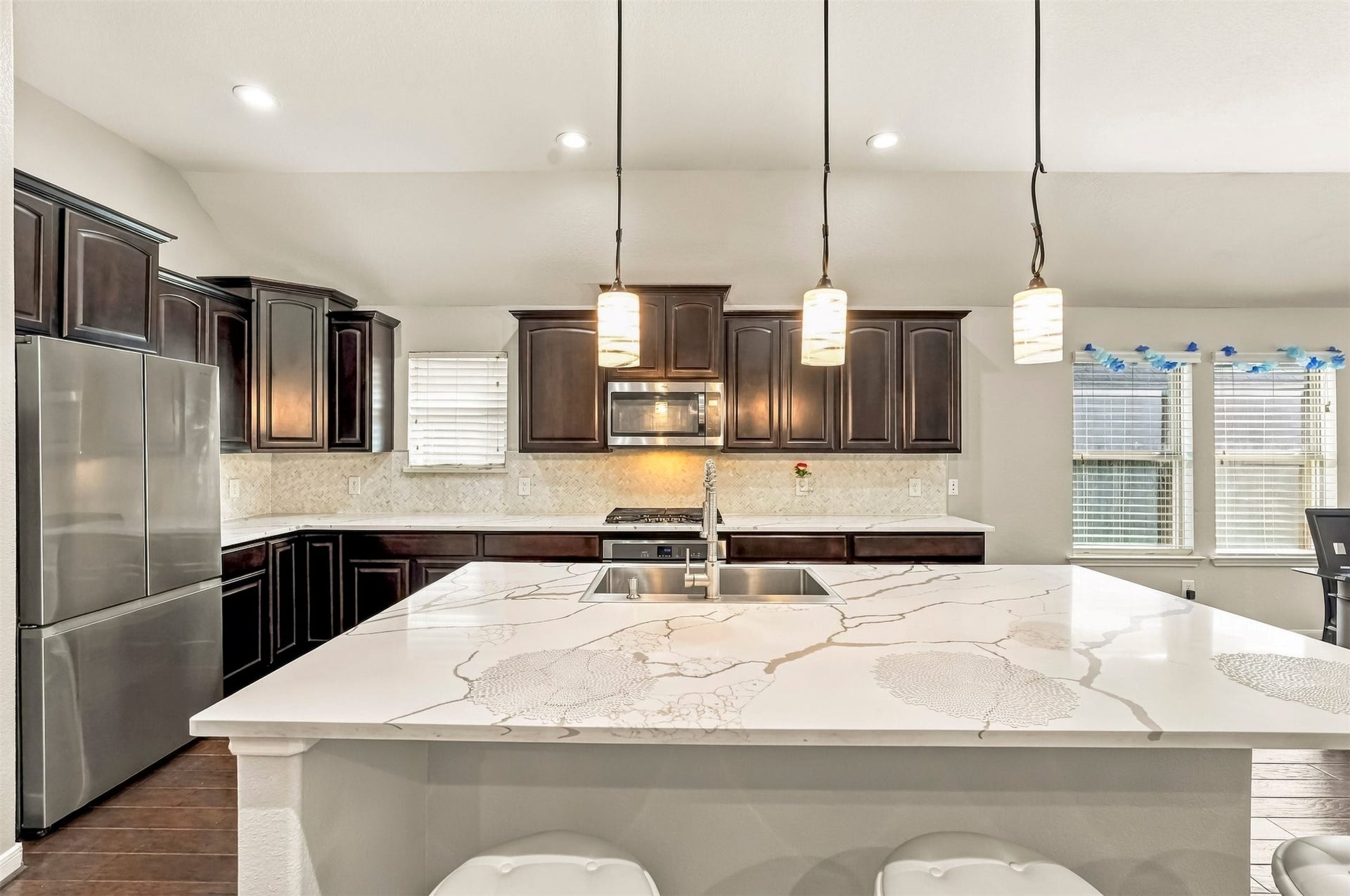 4557 Argonne Woods Drive, Porter, TX 77365 Elegant kitchen featuring dark wooden cabinetry, a sleek stainless steel refrigerator, and a spacious marble island with modern pendant lighting.