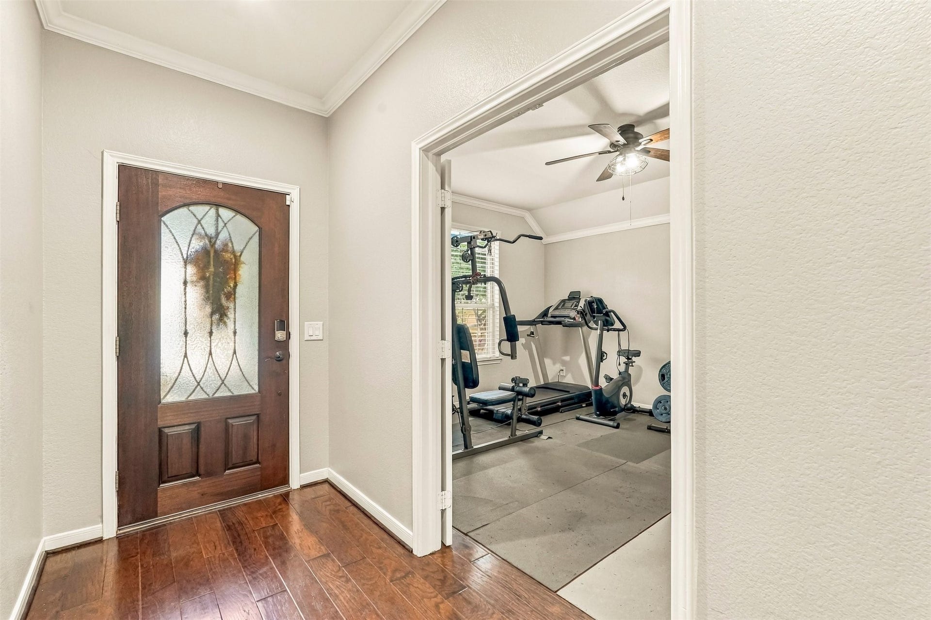 4557 Argonne Woods Drive, Porter, TX 77365 Inviting entryway with rich hardwood floors and a stylish glass-paneled door, leading to a versatile room equipped as a home gym.