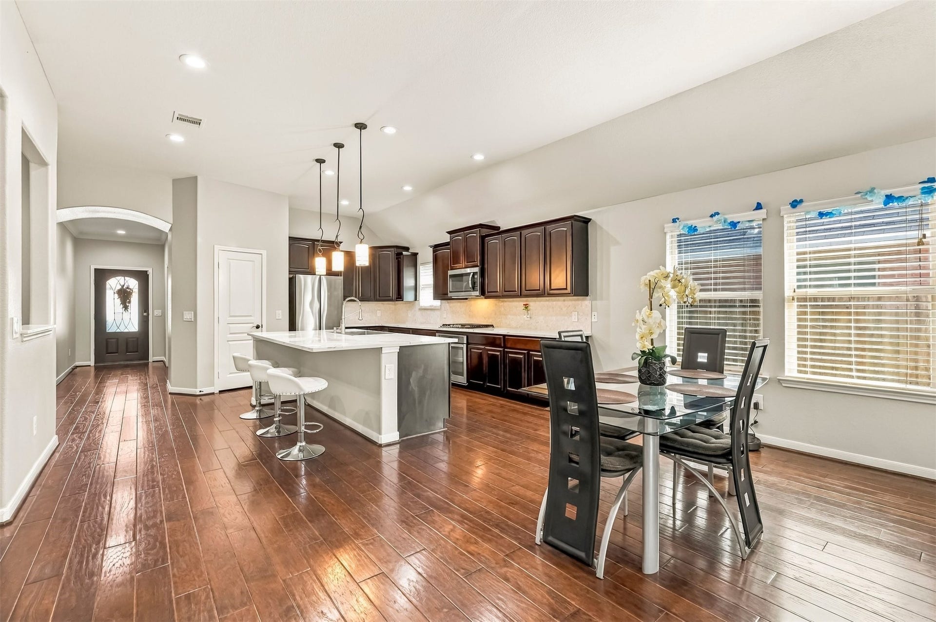 4557 Argonne Woods Drive, Porter, TX 77365 Spacious open-concept kitchen and dining area featuring elegant hardwood floors, a modern island with bar seating, sleek stainless steel appliances, and rich dark cabinetry. Natural light fills the space through large windows, creating a warm and inviting atmosphere.