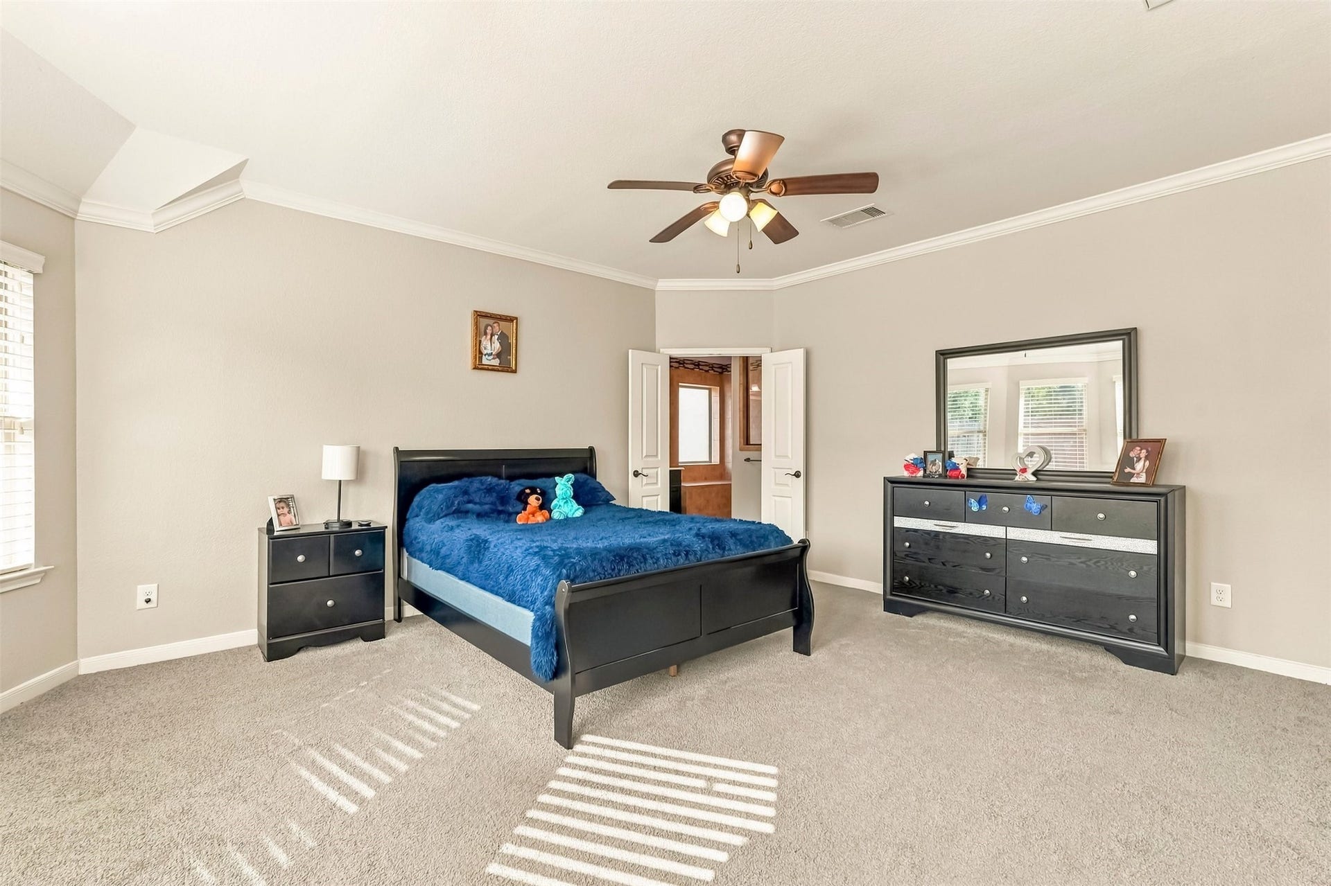 4557 Argonne Woods Drive, Porter, TX 77365 Spacious bedroom with neutral tones features a comfortable bed, plush carpet, and ample natural light, complemented by modern furniture and a ceiling fan for added comfort.