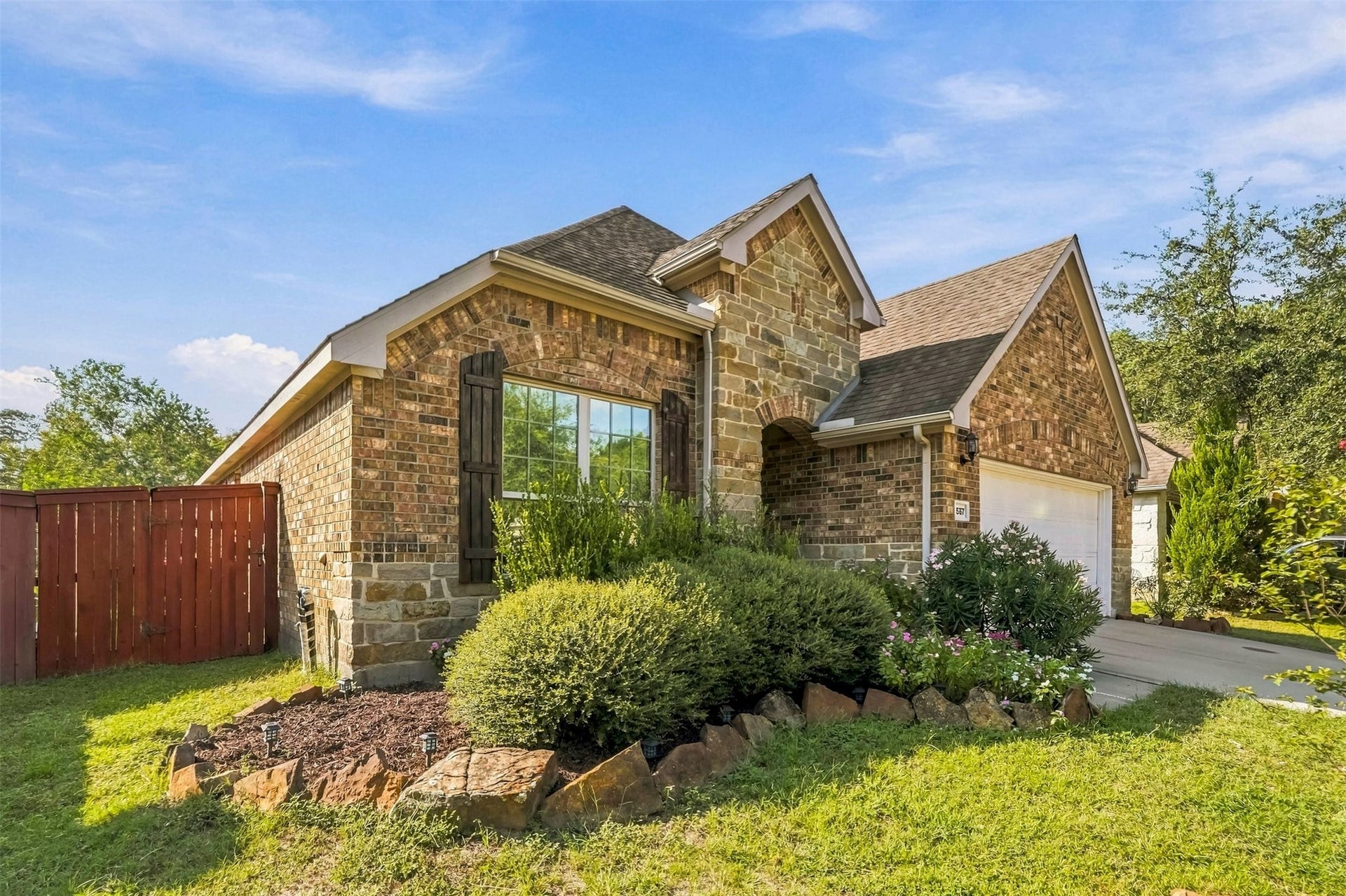 4557 Argonne Woods Drive, Porter, TX 77365 Charming brick home with rustic stone accents and a well-maintained front garden. The property features a spacious driveway leading to a two-car garage and a fenced yard for added privacy.