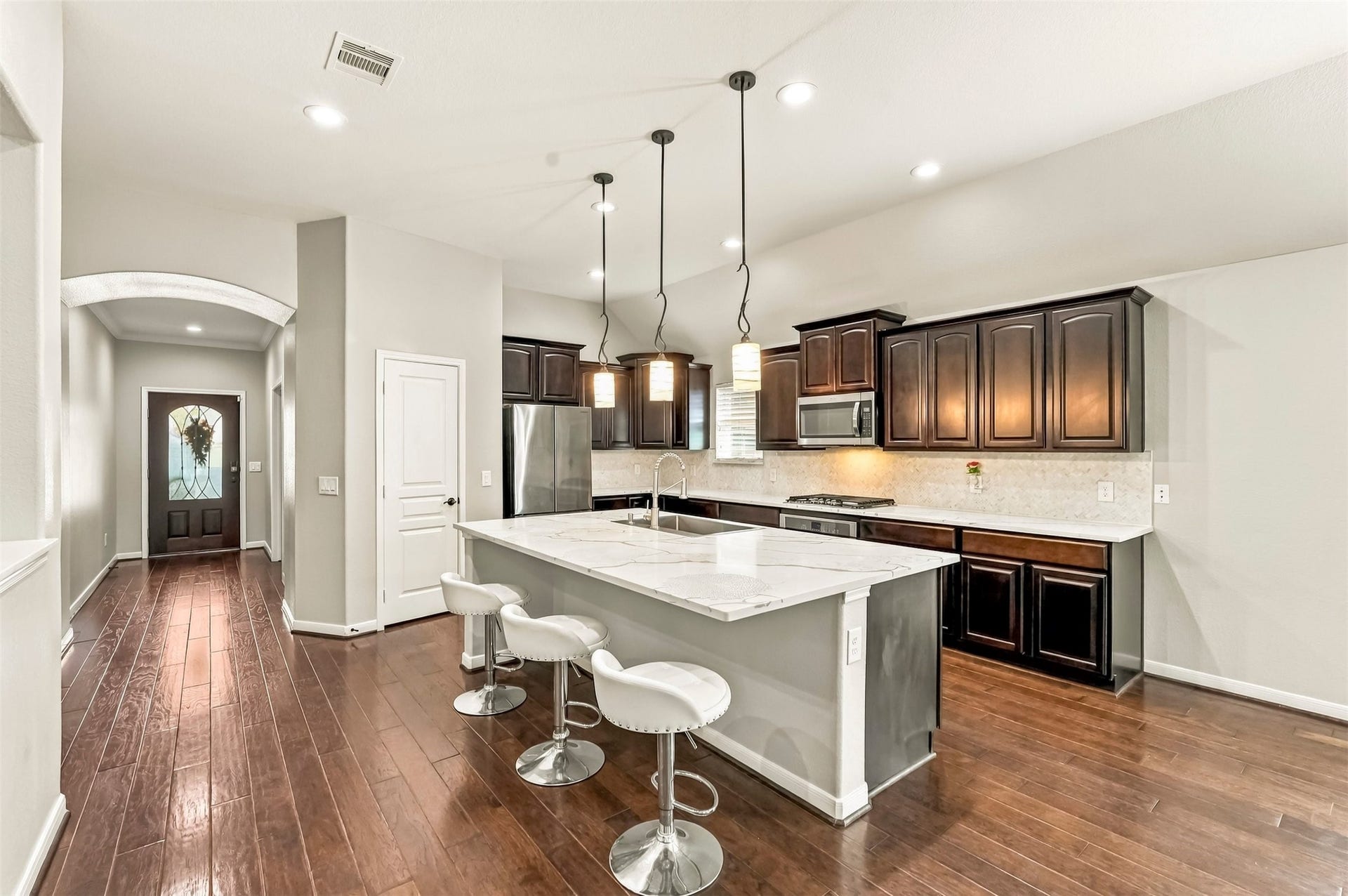 4557 Argonne Woods Drive, Porter, TX 77365 Spacious kitchen with elegant dark cabinetry, a large marble island with seating, and modern stainless steel appliances, complemented by warm wood flooring and recessed lighting.