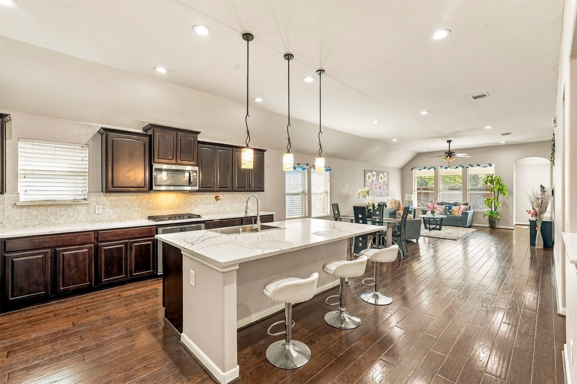 4557 Argonne Woods Drive, Porter, TX 77365 Spacious open-concept kitchen and living area featuring elegant dark wood cabinetry, a large marble island with seating, and stylish pendant lighting, seamlessly flowing into a cozy, well-lit living room with large windows and hardwood floors.