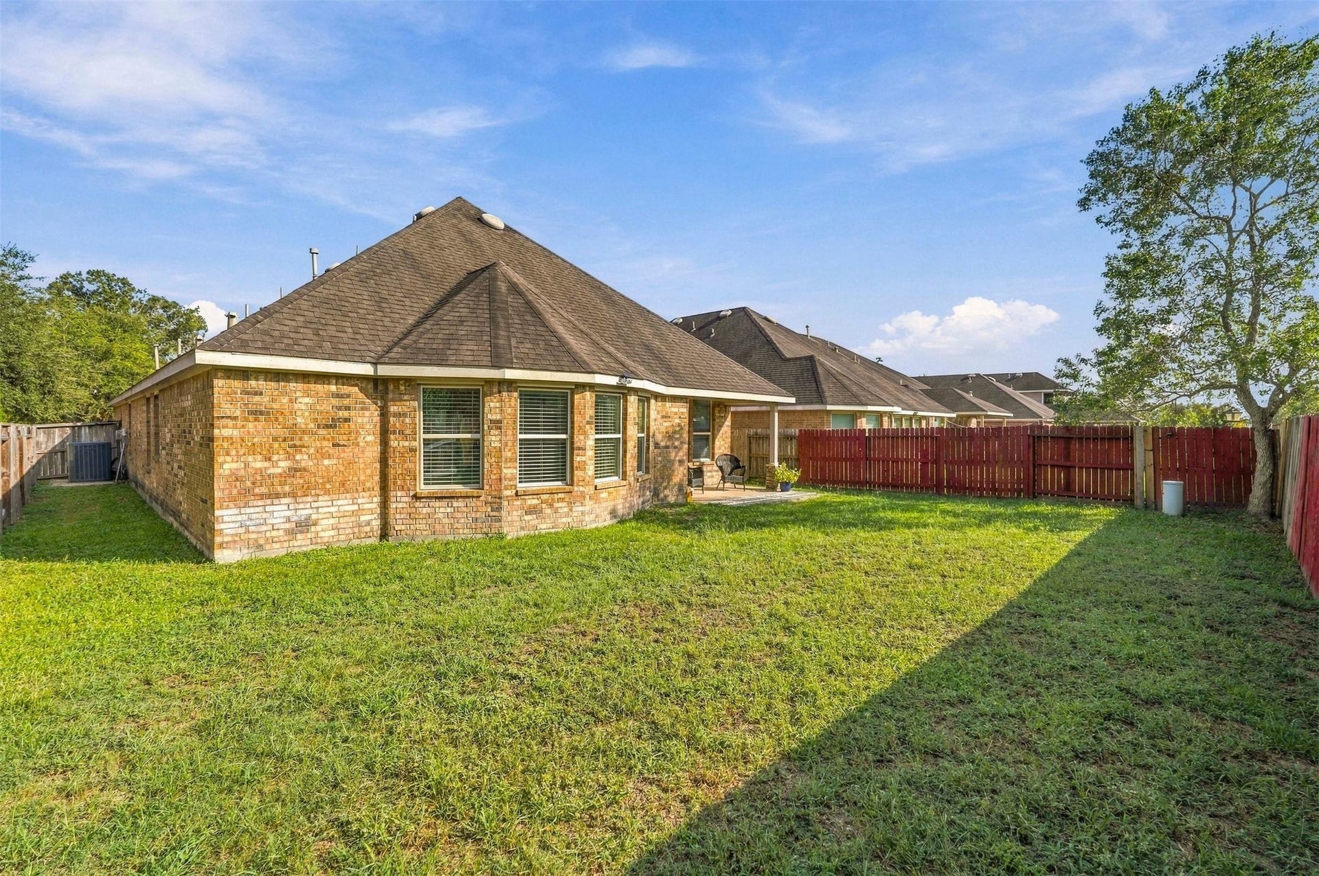 4557 Argonne Woods Drive, Porter, TX 77365 Spacious backyard with lush grass, bordered by a charming brick exterior and a red wooden fence, perfect for outdoor activities and relaxation.