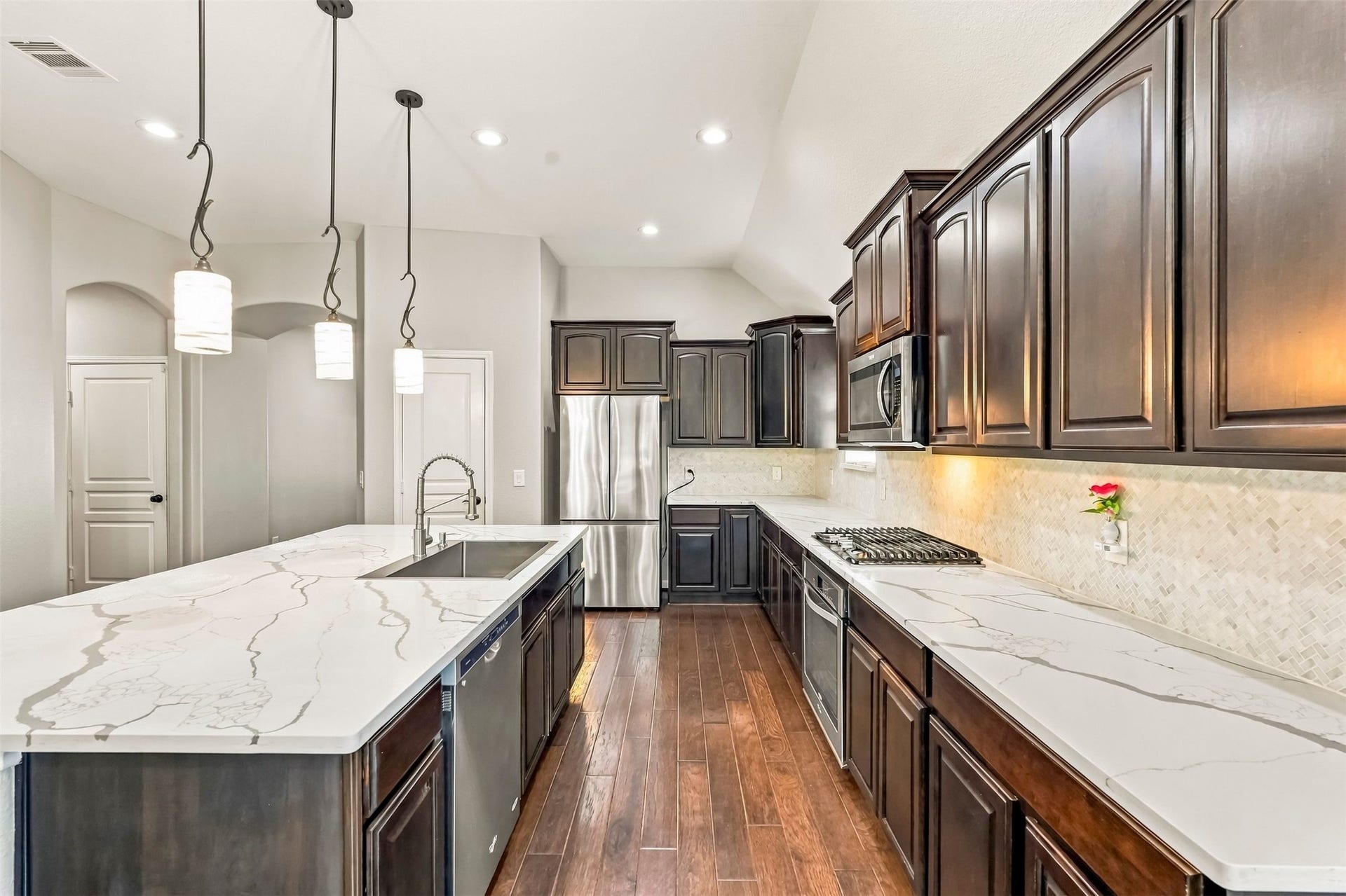 4557 Argonne Woods Drive, Porter, TX 77365 Sleek kitchen featuring dark wood cabinetry, elegant white marble countertops, and modern stainless steel appliances, illuminated by stylish pendant lighting.