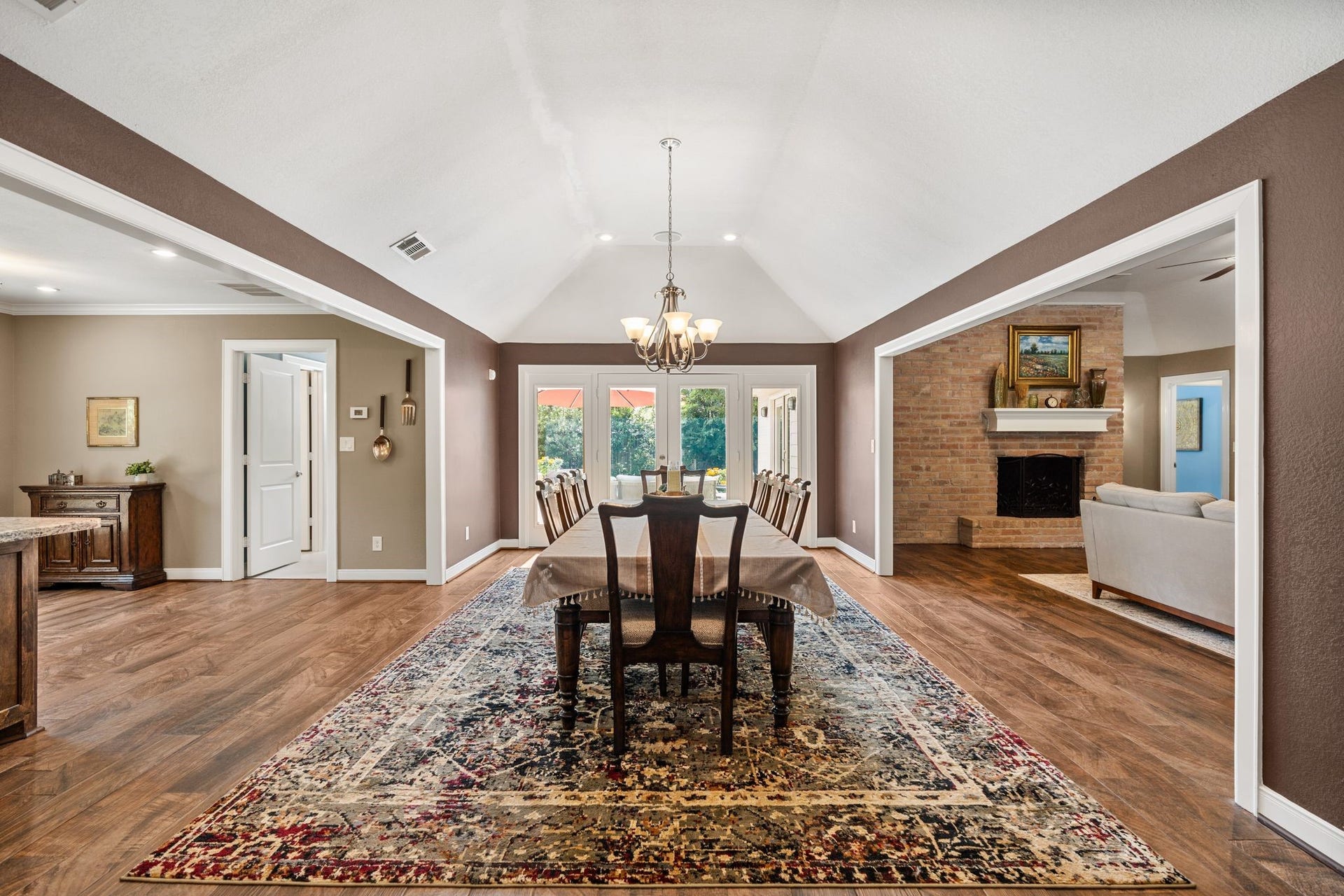 11519 Lakeside Place Drive, Houston, TX 77077 Spacious dining area with vaulted ceilings, elegant chandelier, and a rich hardwood floor, seamlessly connecting to a cozy living room with a brick fireplace.