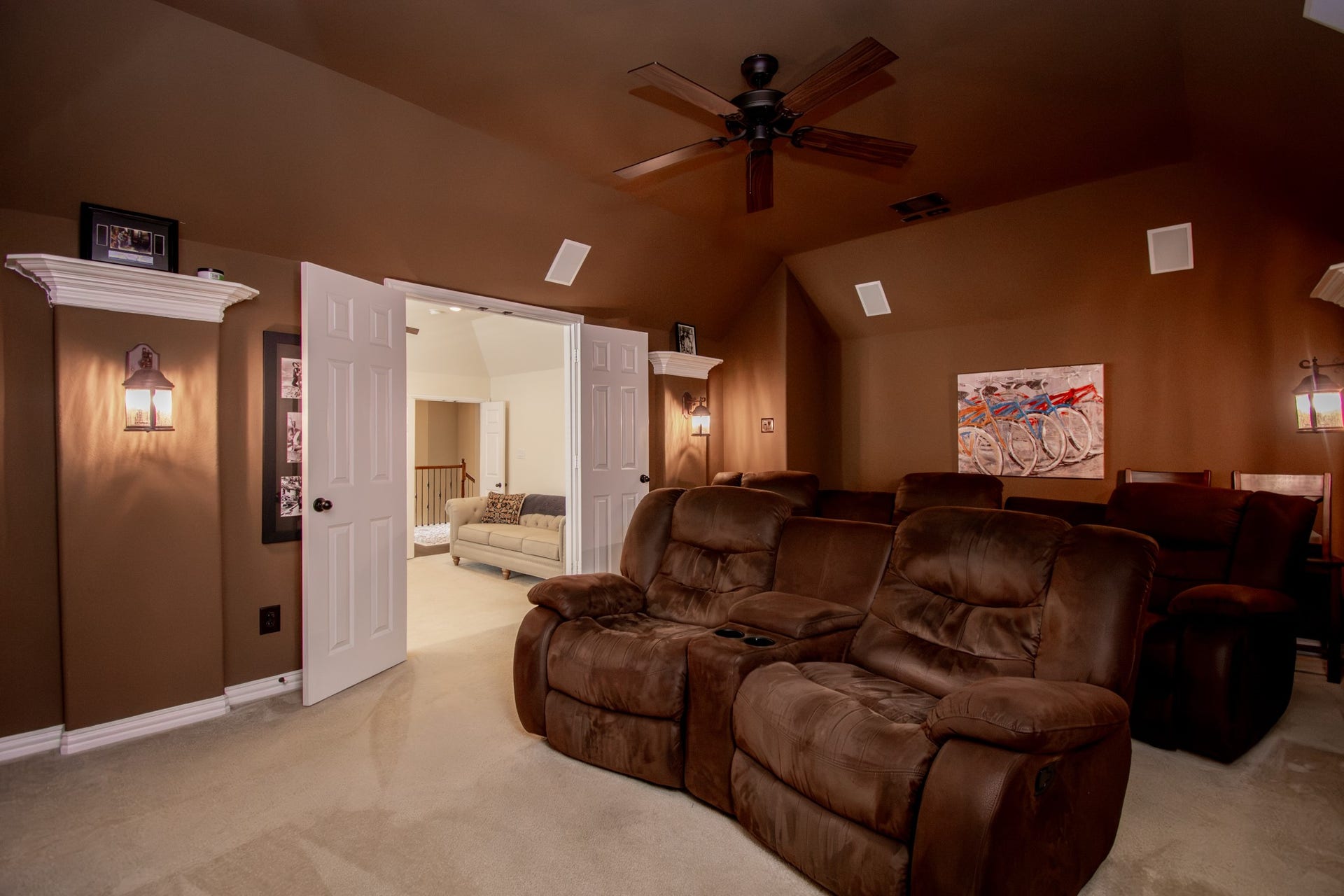 Front view of Media room looking back into the game room. Sconces on walls along with speakers add to the feel of a true media room.